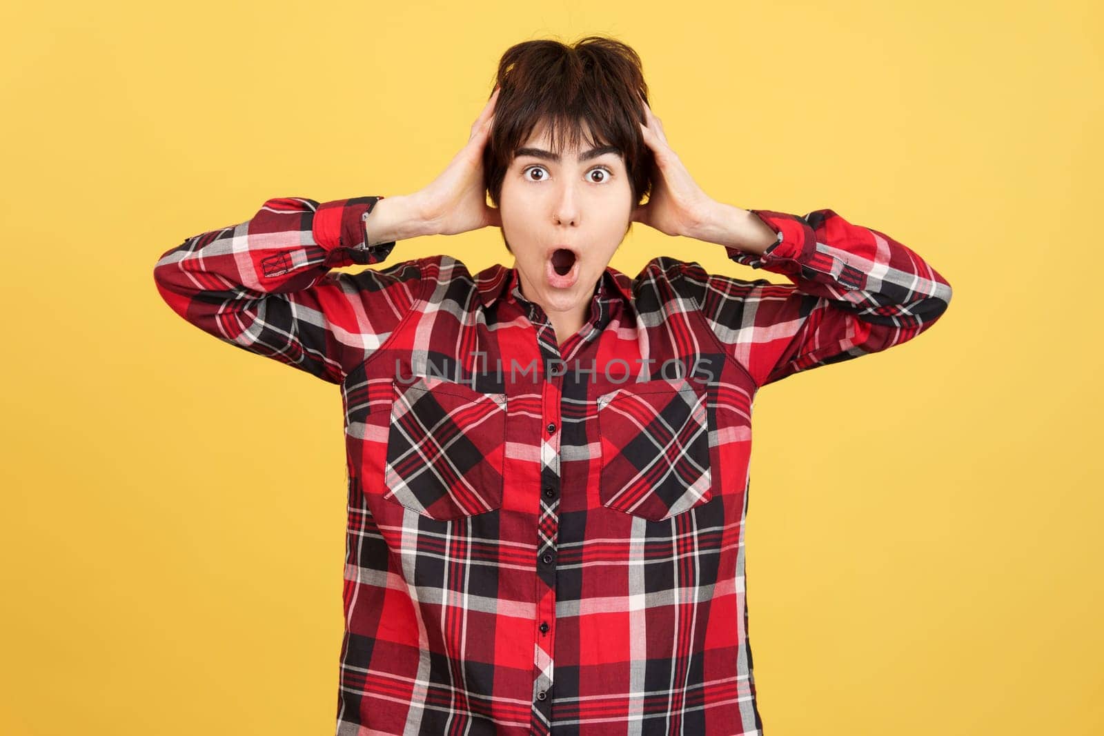 Cool Androgynous person looking at camera while expressing surprise in studio with yellow background
