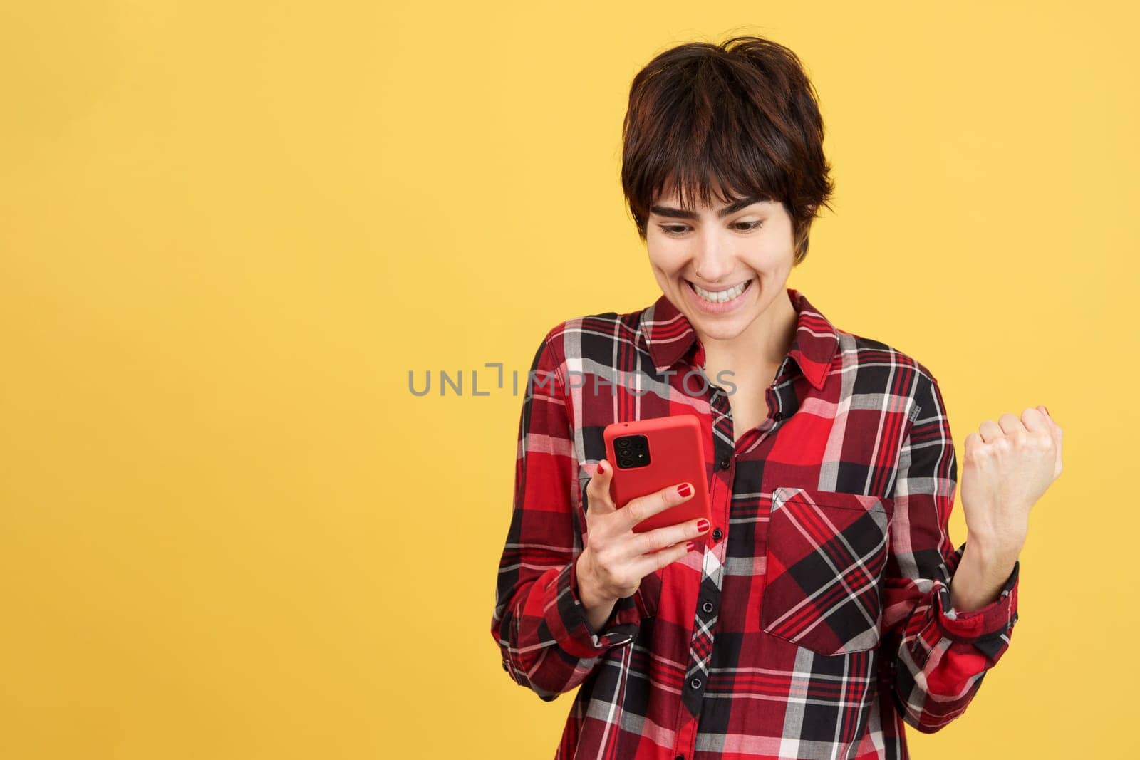 Androgynous person celebrating while using a mobile in studio with yellow background
