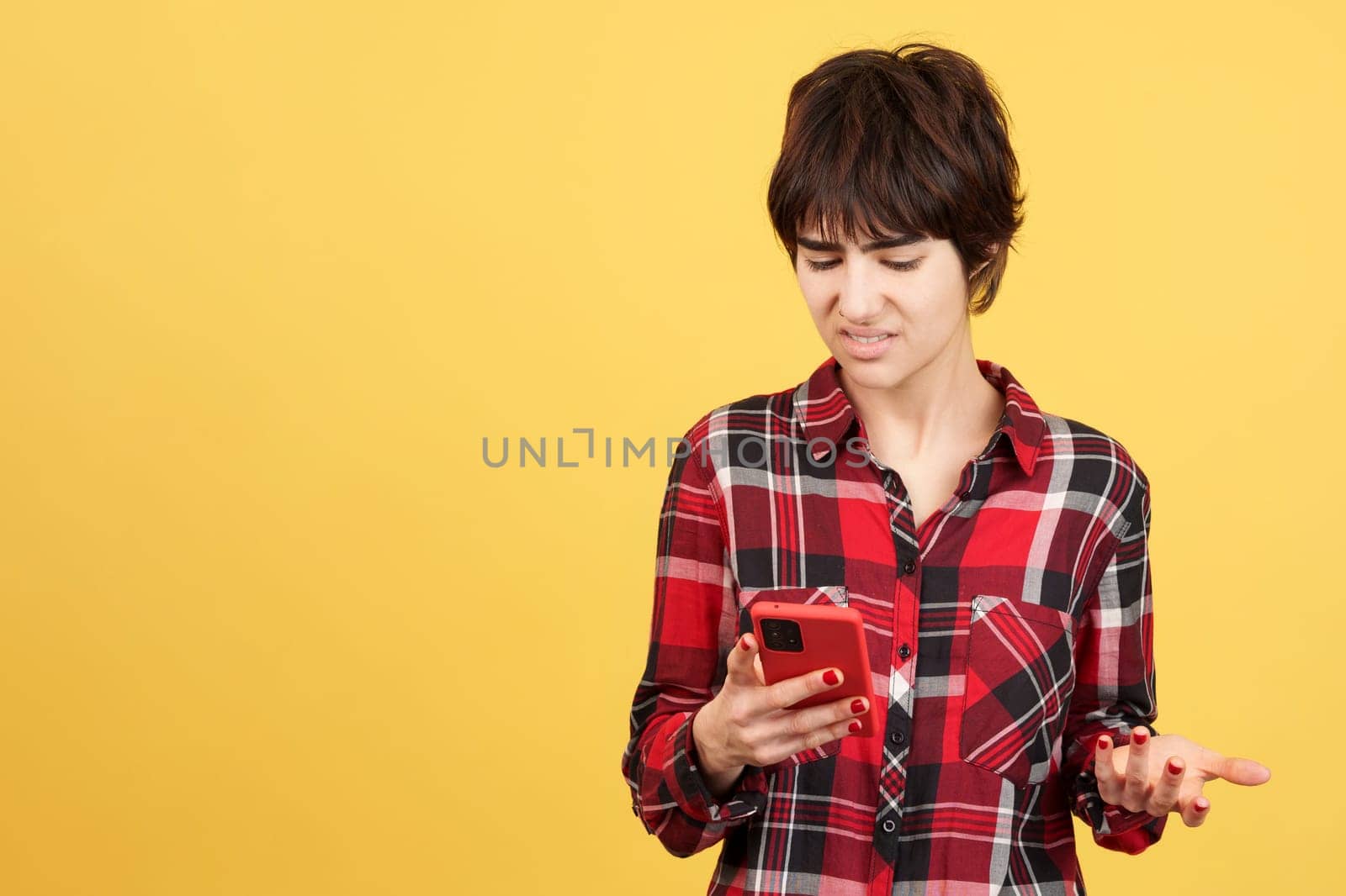 Angry androgynous person using a mobile phone in studio with yellow background