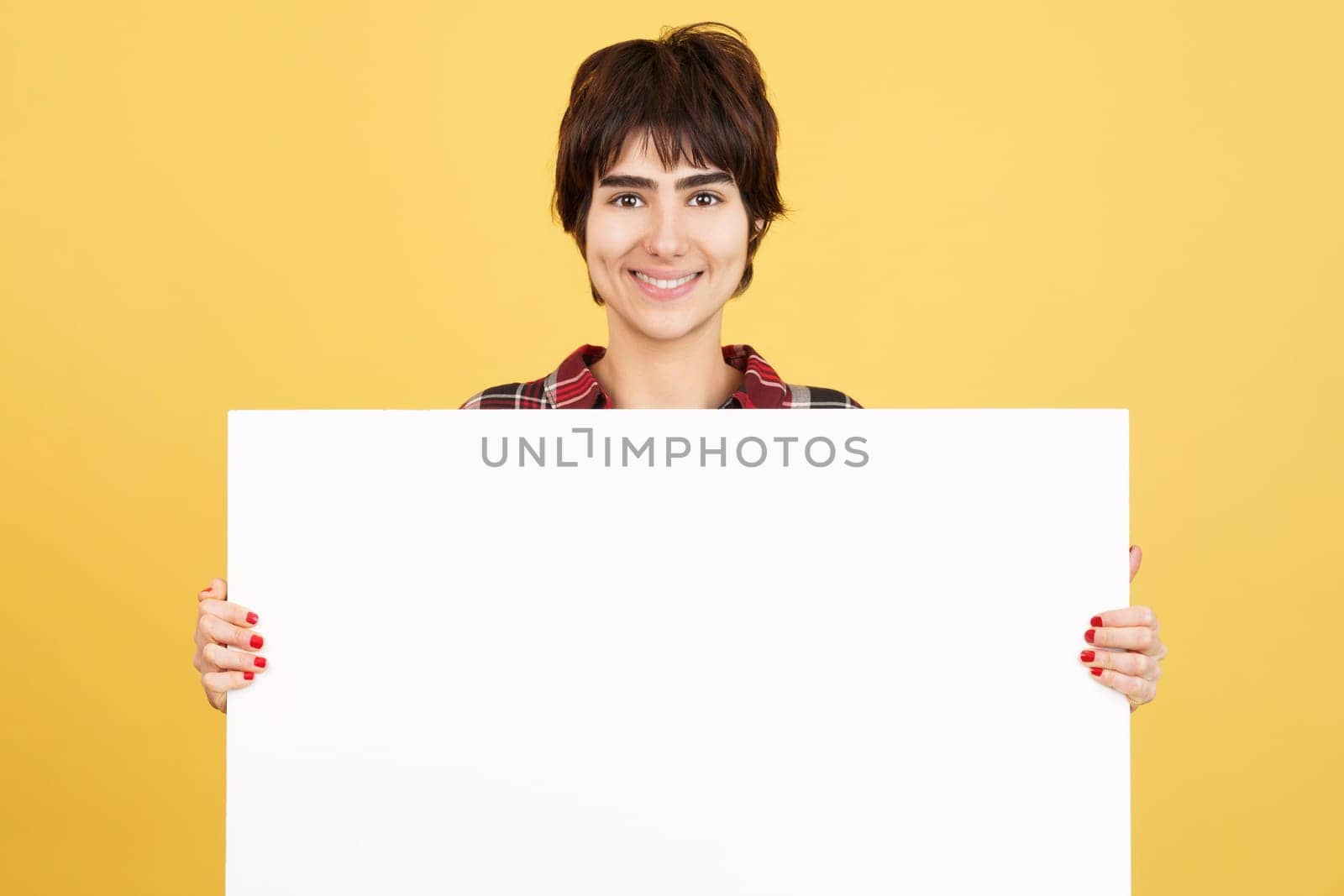 Androgynous person holding a blank panel while smiling in studio with yellow background