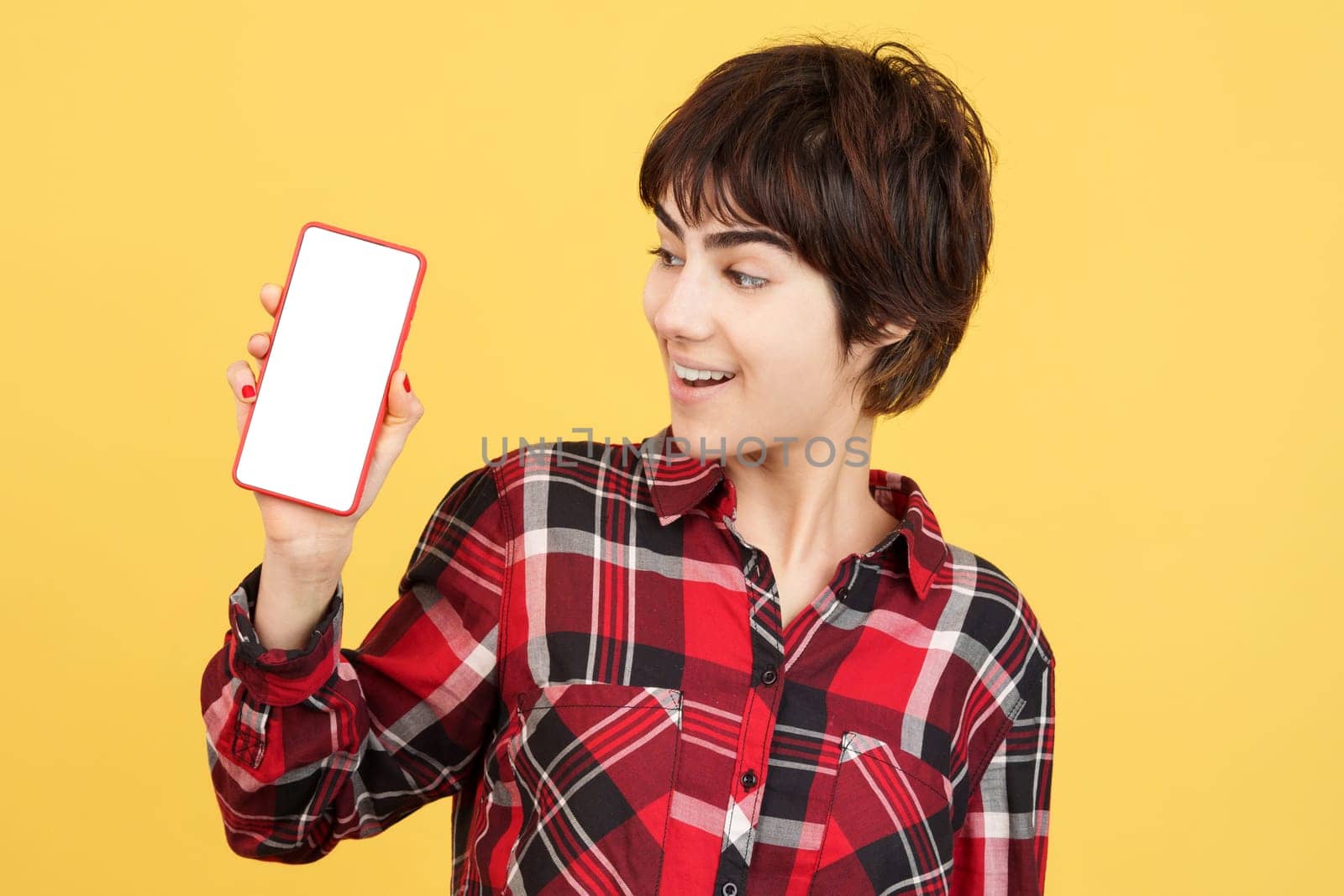 Androgynous person looking to a blank mobile screen in studio with yellow background