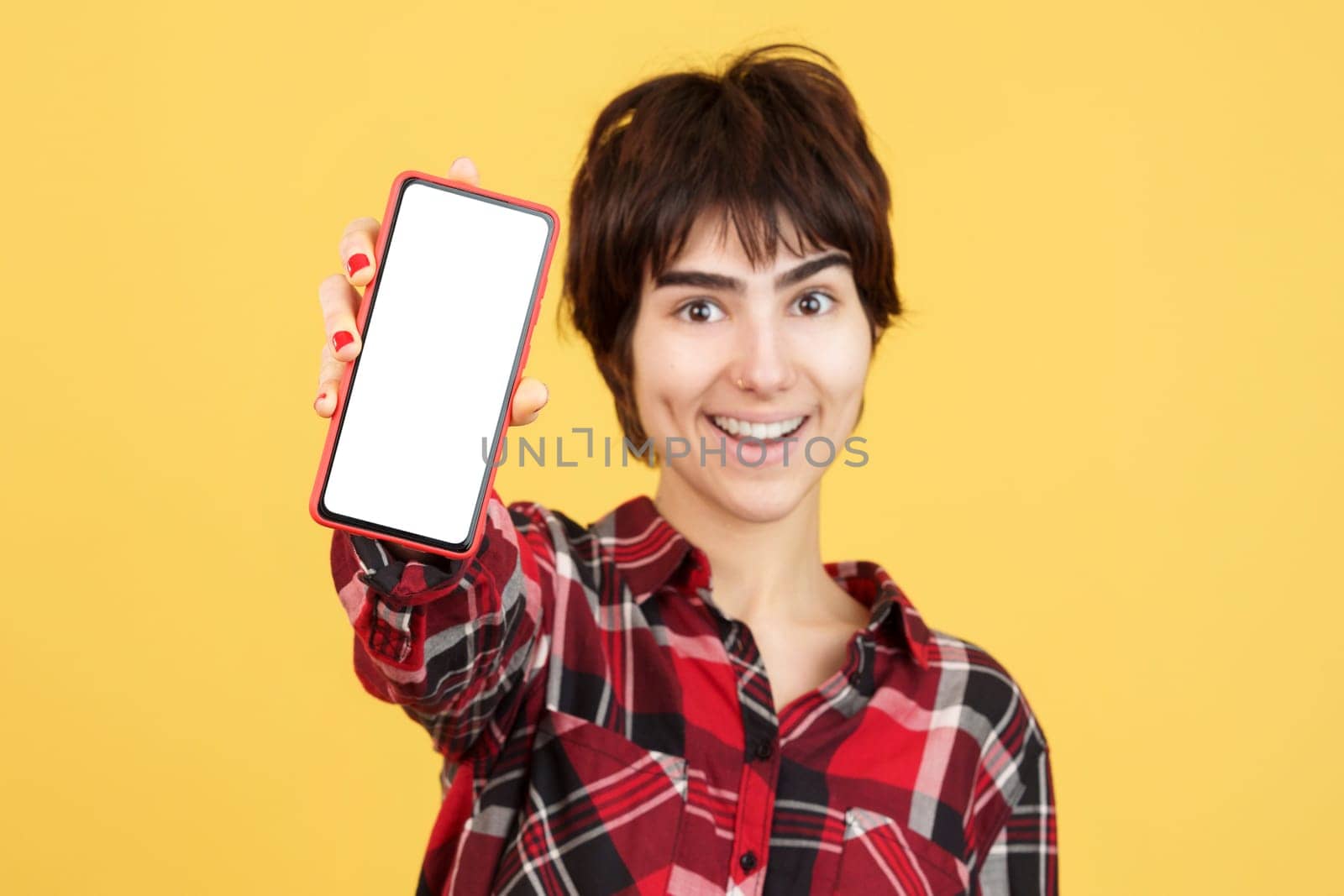 Androgynous person showing a blank mobile screen in studio with yellow background