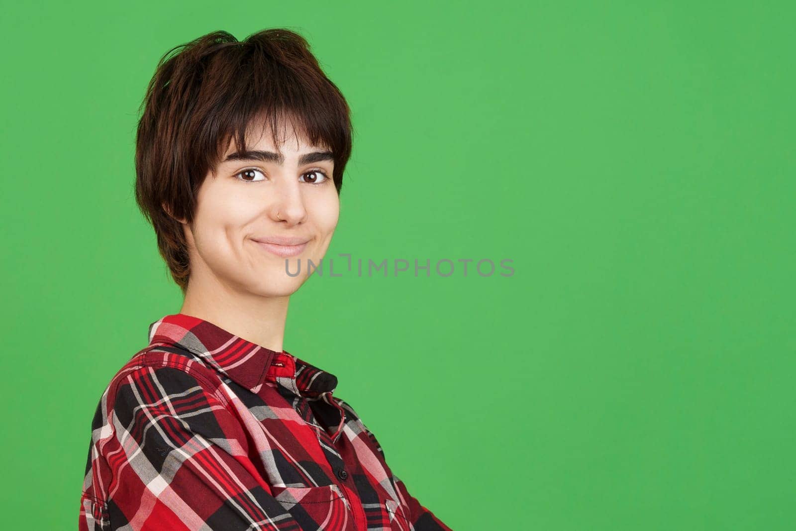 Androgynous person looking at the camera and smiling in studio with green background