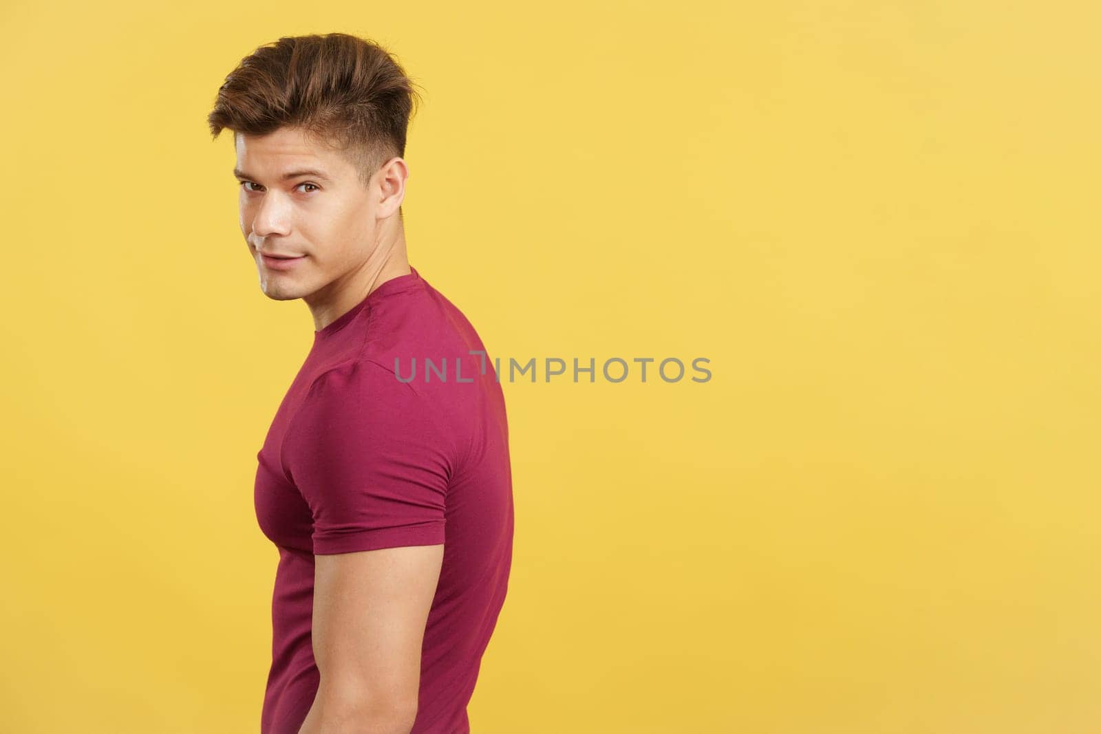 Strong man turning to look at the camera in studio with yellow background