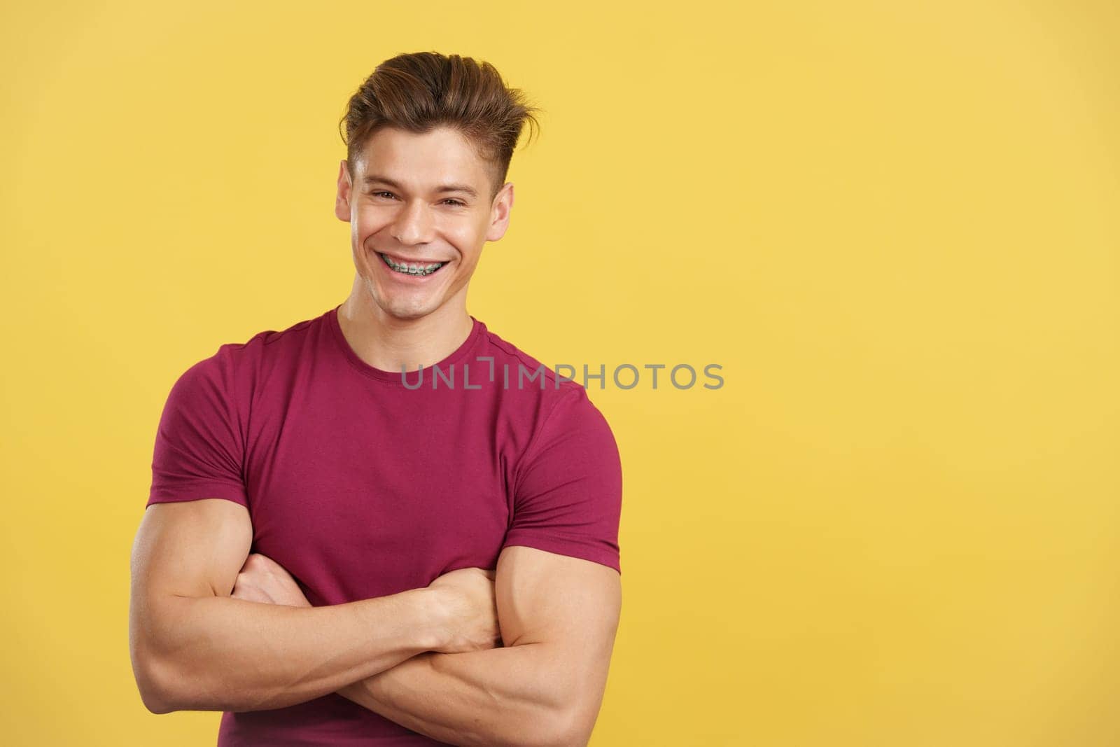 Handsome man with brackets smiling at camera in studio with yellow background