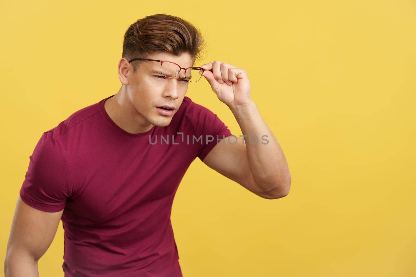 Strong man taking off her glasses to see far away in studio with yellow background