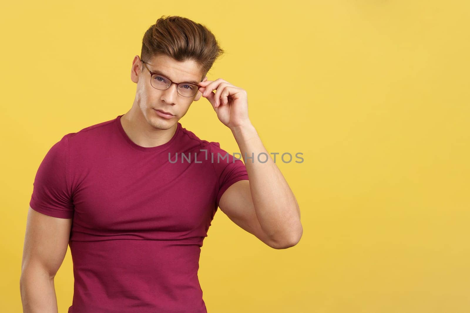 Sensual student taking off the eyeglasses while looking at camera in studio with yellow background