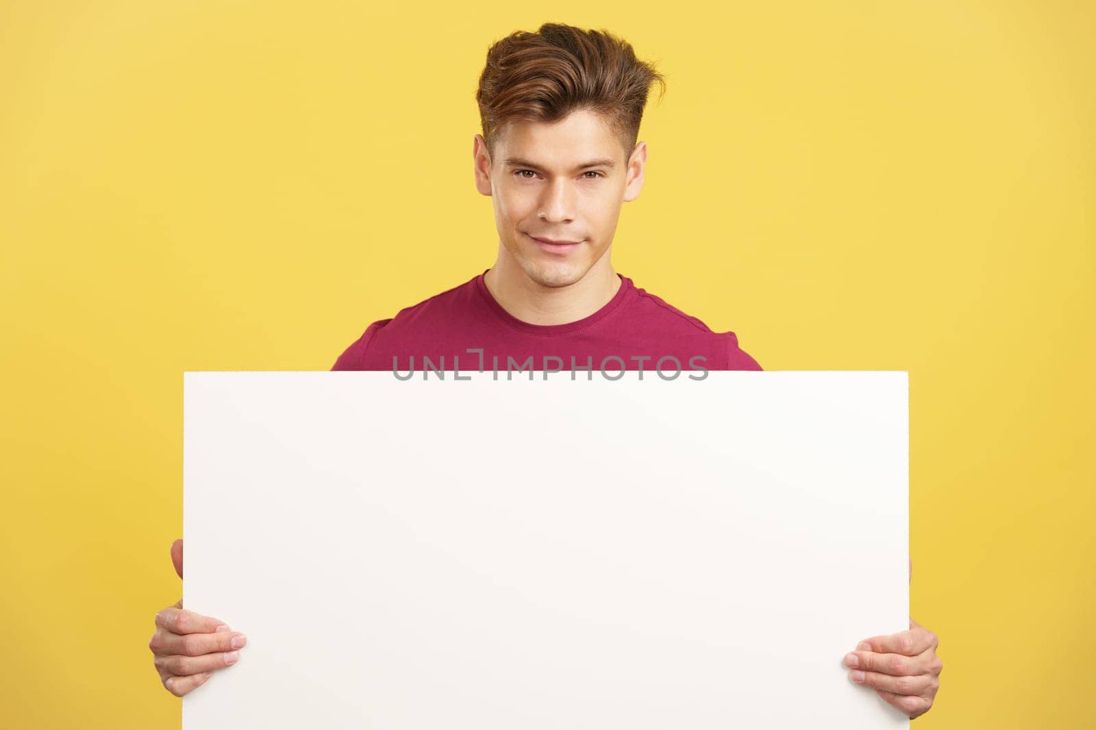 Man holding a blank panel while smiling at the camera in studio with yellow background