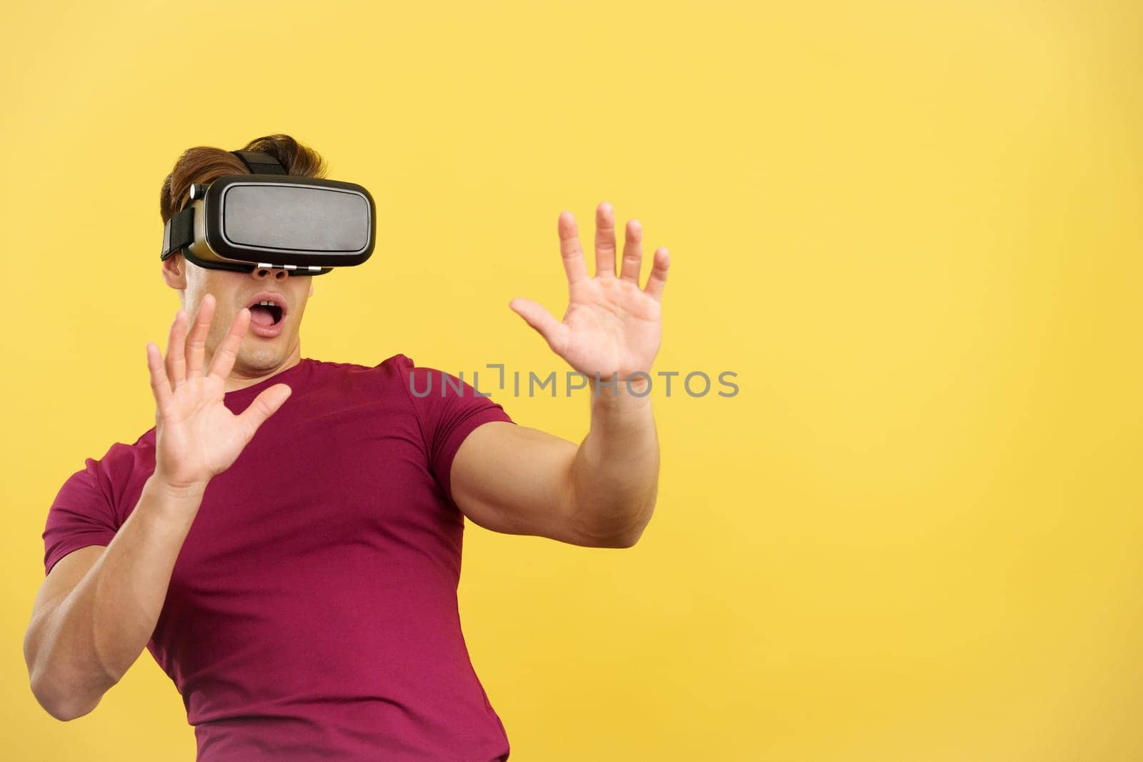 Surprised strong man with Virtual Reality goggles in studio with yellow background