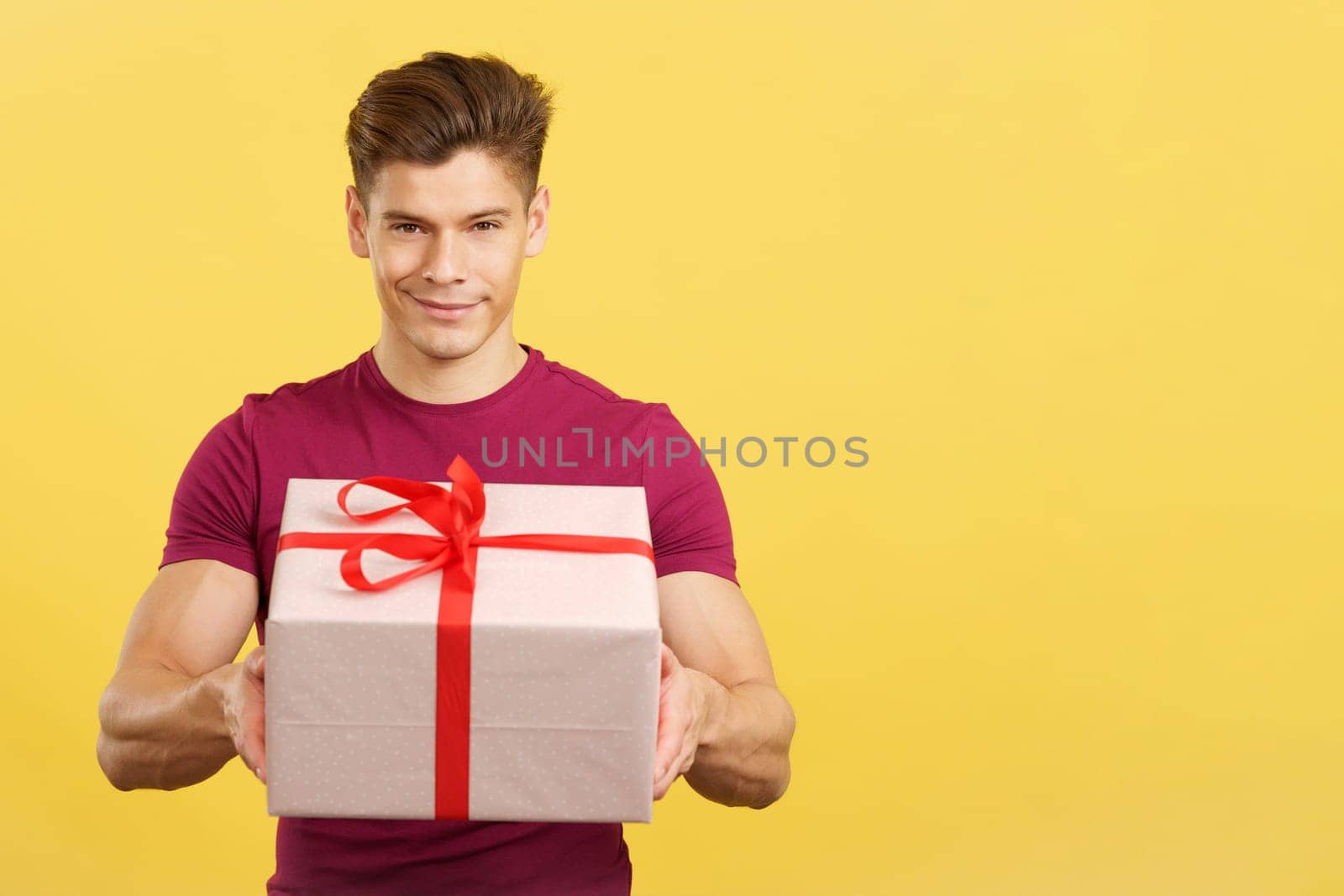 Happy man looking at the camera giving a present in studio with yellow background