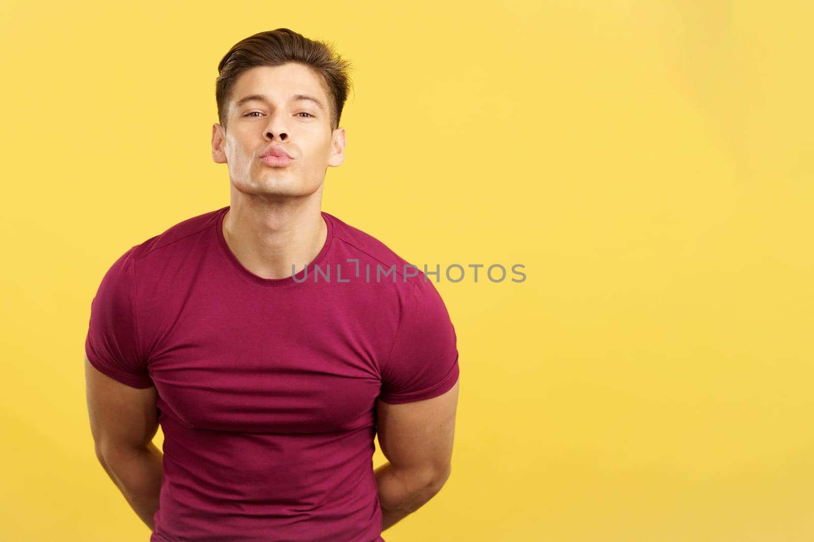 Sensual and strong man kissing while looking at camera in studio with yellow background