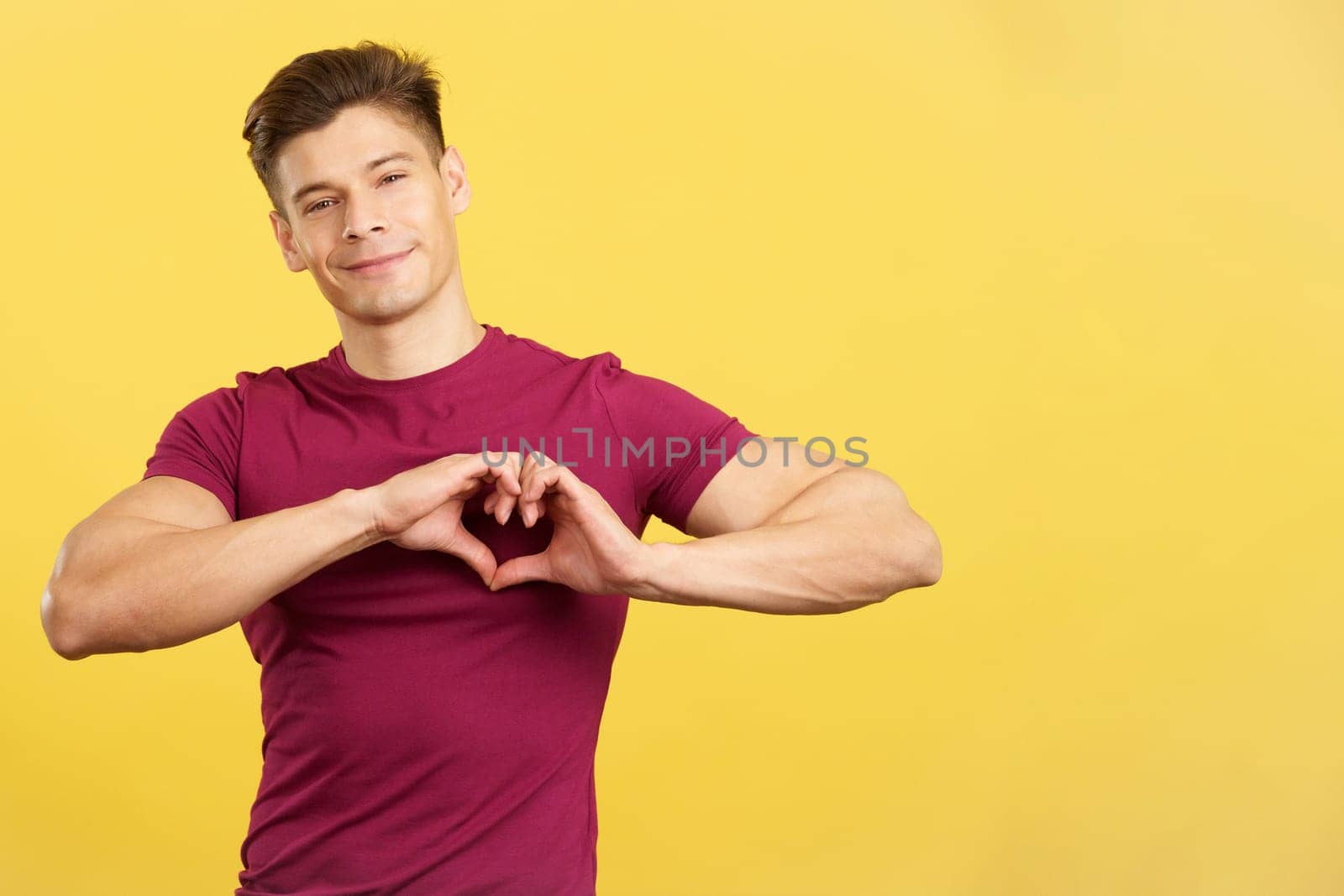 Man representing a heart shape with the hands in studio with yellow background