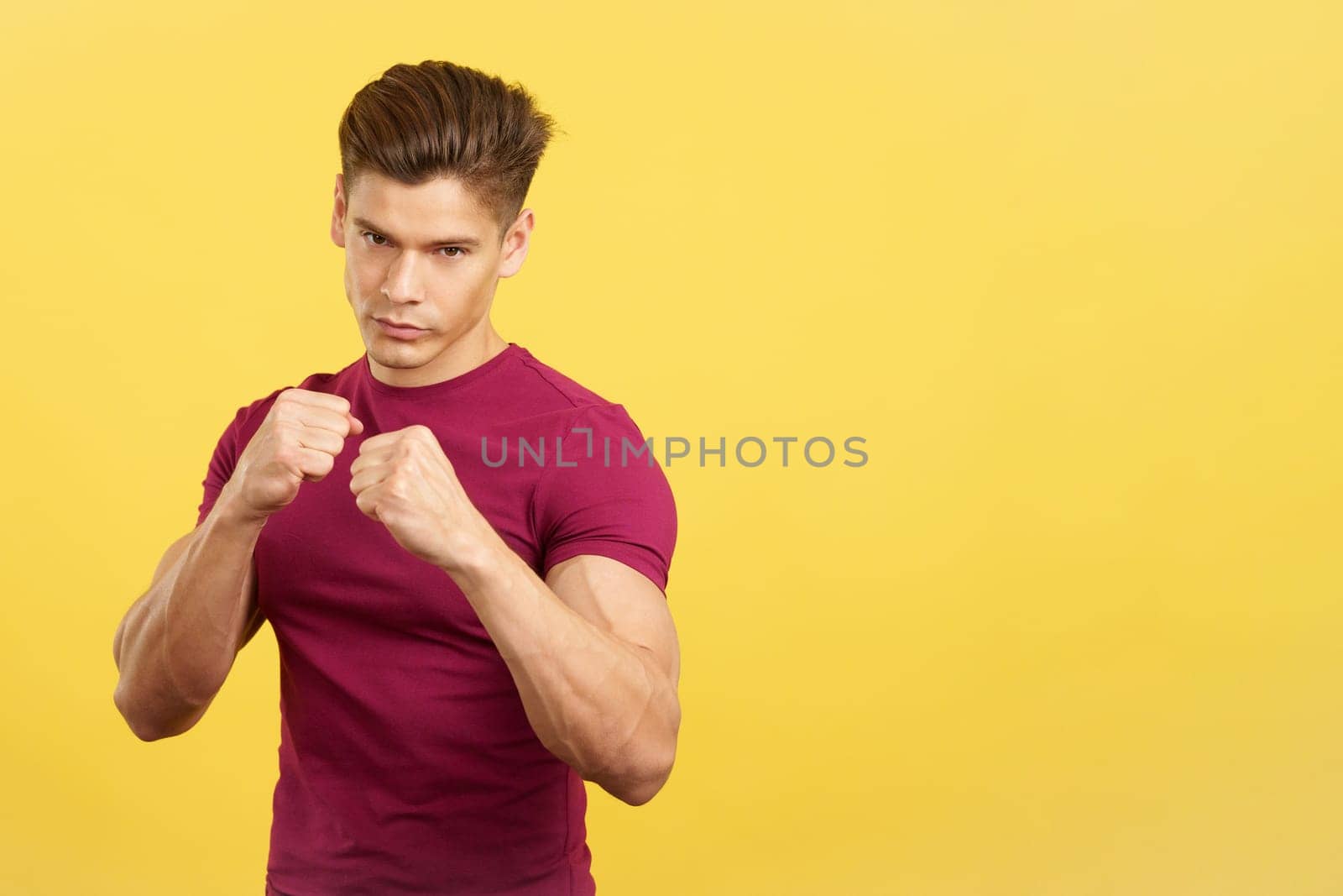Serious man in guard pose of boxing looking at camera in studio with yellow background