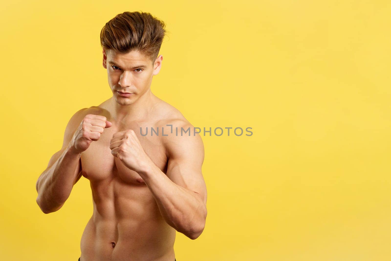 Strong male boxer standing with bare torso in studio with yellow background