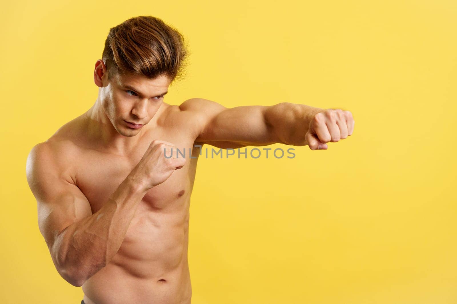 Strong man doing shadow boxing with bare torso in studio with yellow background