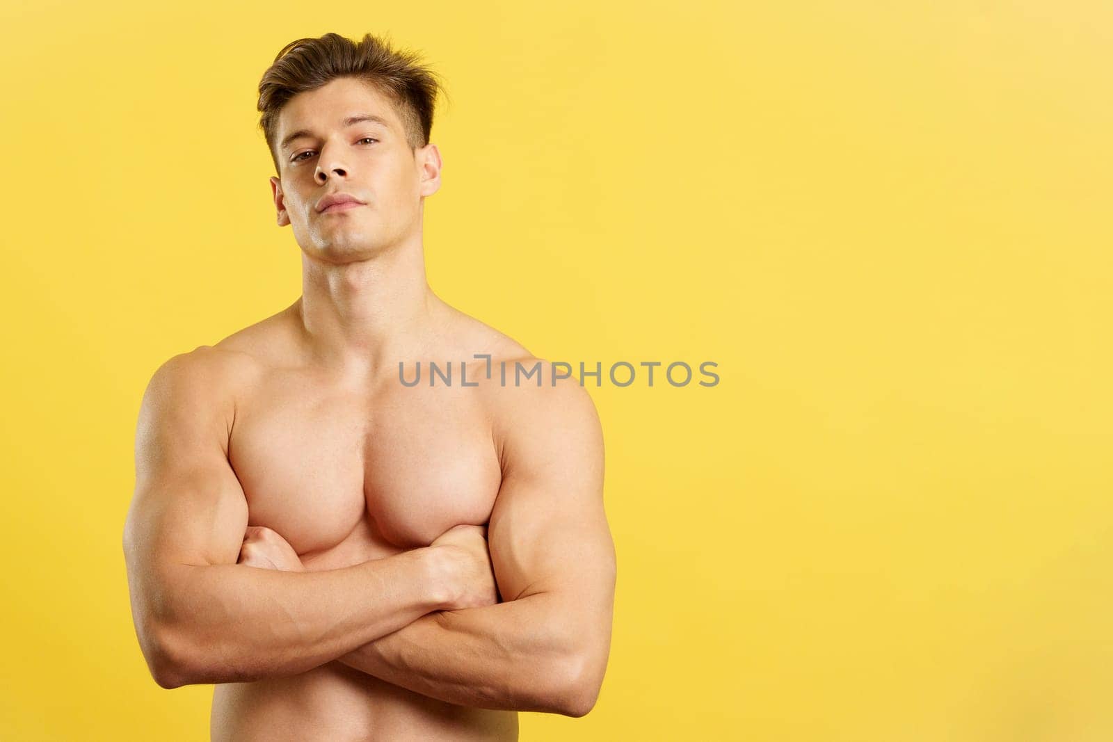 Proud strong man looking at camera shirtless in studio with yellow background