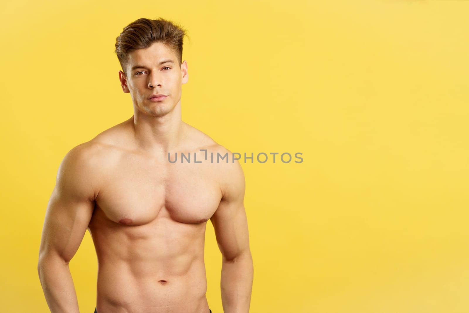 Strong caucasian man standing looking at camera in studio with yellow background