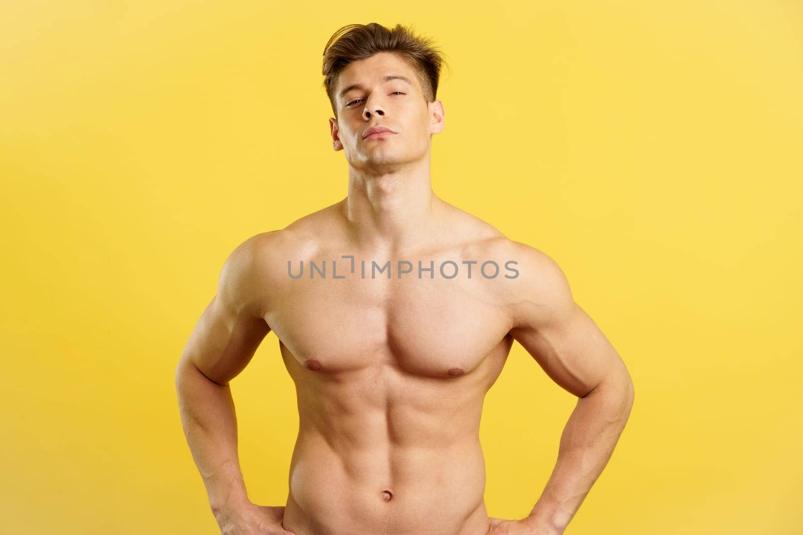 Strong and sensual nude man looking at camera in studio with yellow background