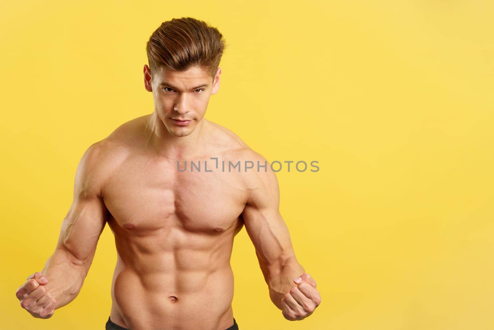 Strong man with abs looking at camera showing muscle in studio with yellow background