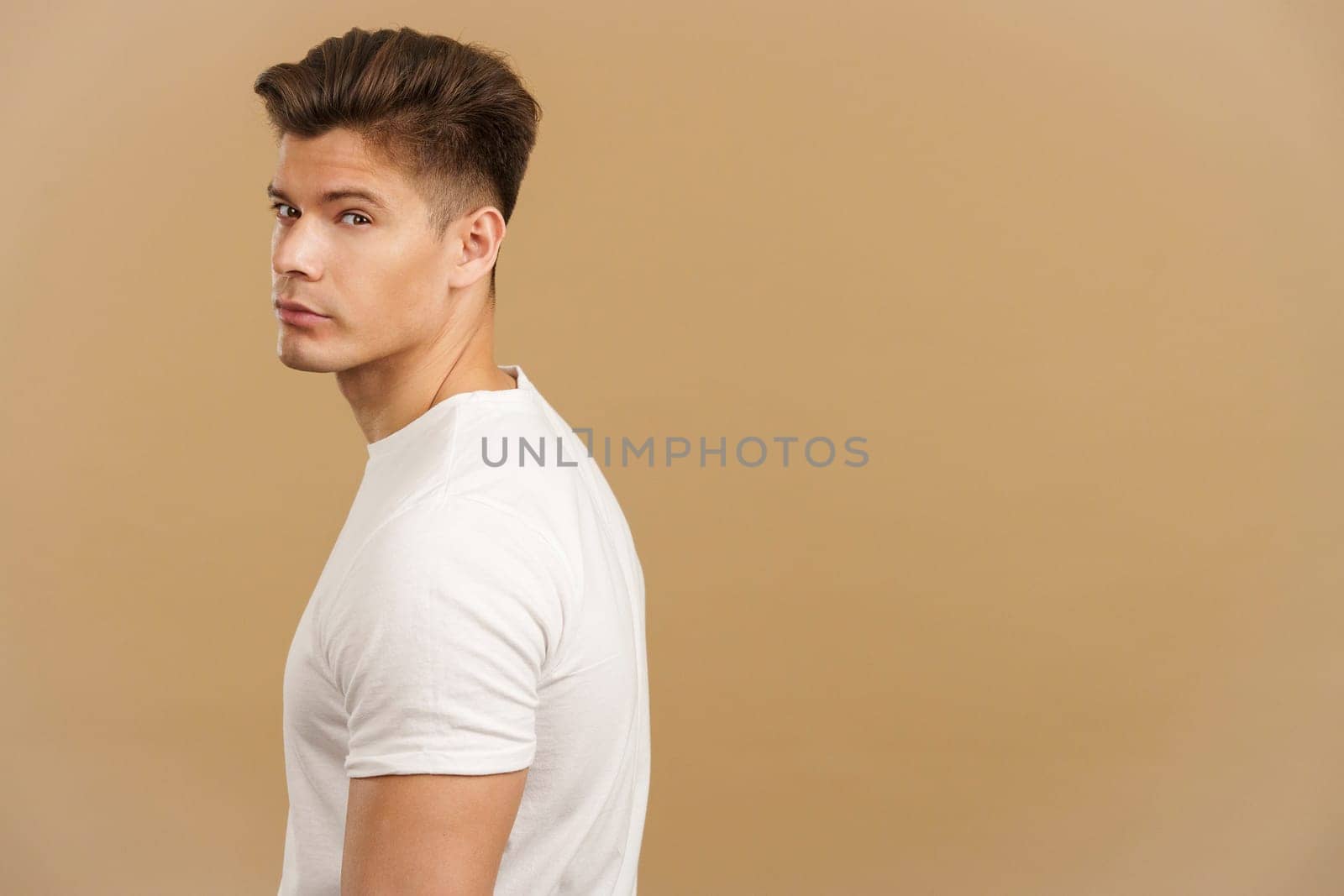 Handsome man turning to looking at camera in studio with brown background