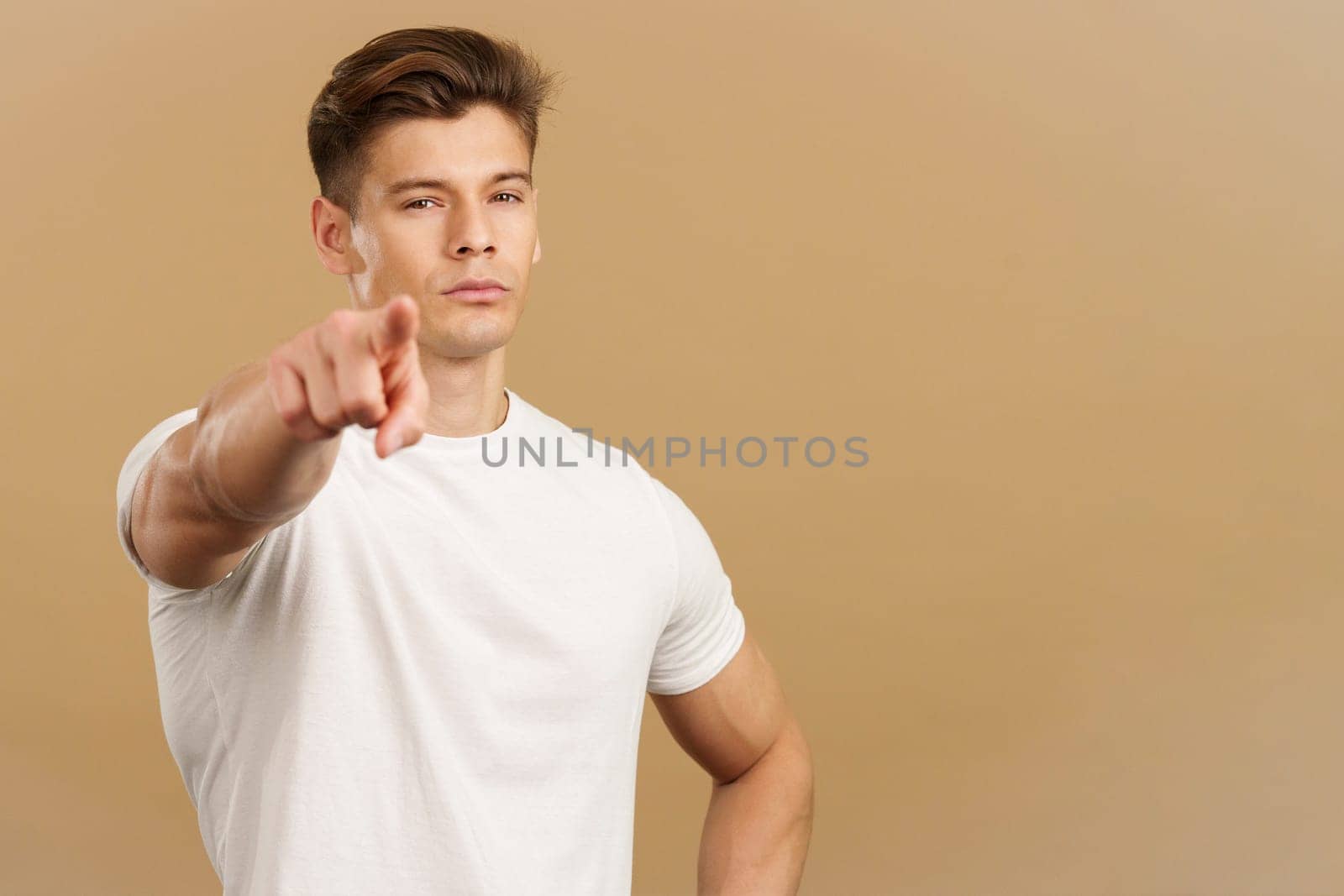 Strong Caucasian man pointing to camera with index finger in studio with brown background