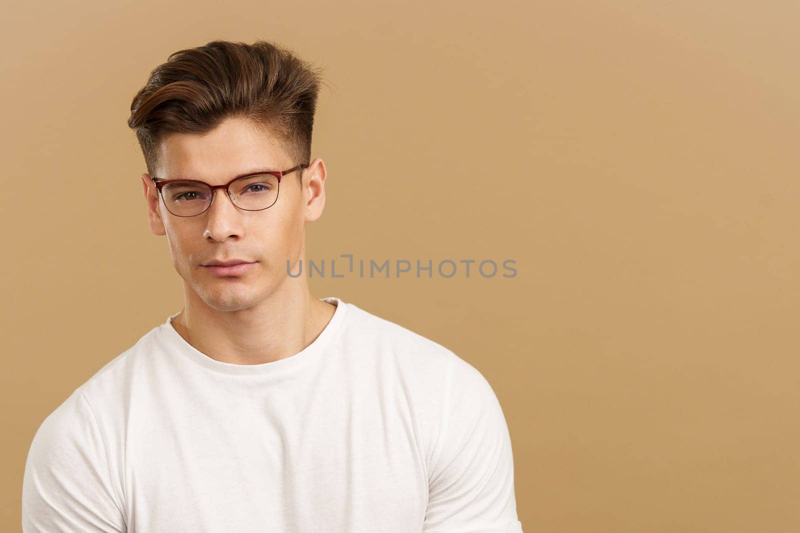 Handsome man with eyeglasses looking at camera in studio with brown background