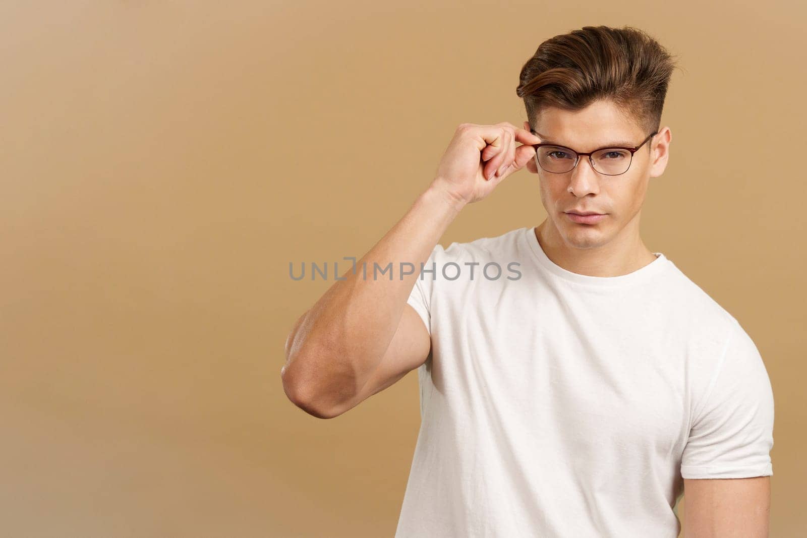 Sensual man taking off the eyeglasses while looking at camera in studio with brown background