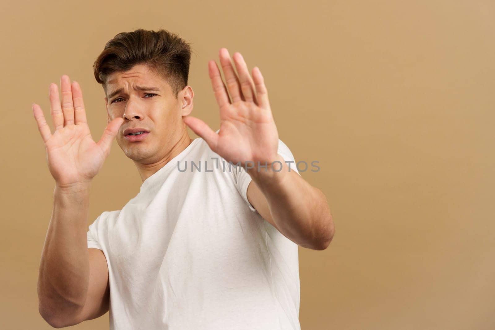 Handsome man gesturing with the hands in fear in studio with brown background