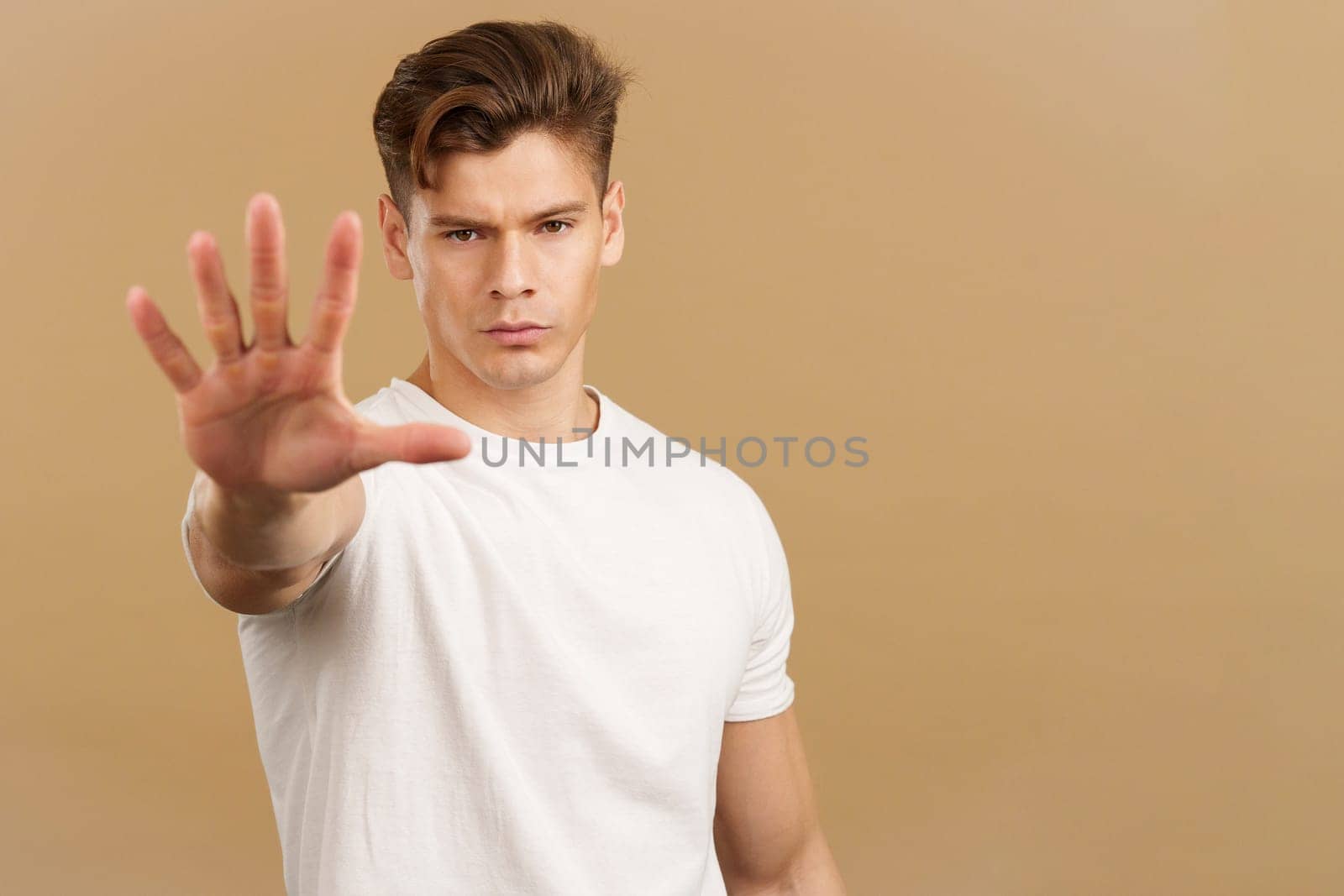 Handsome man gesturing stop with the palm of the hand in studio with brown background