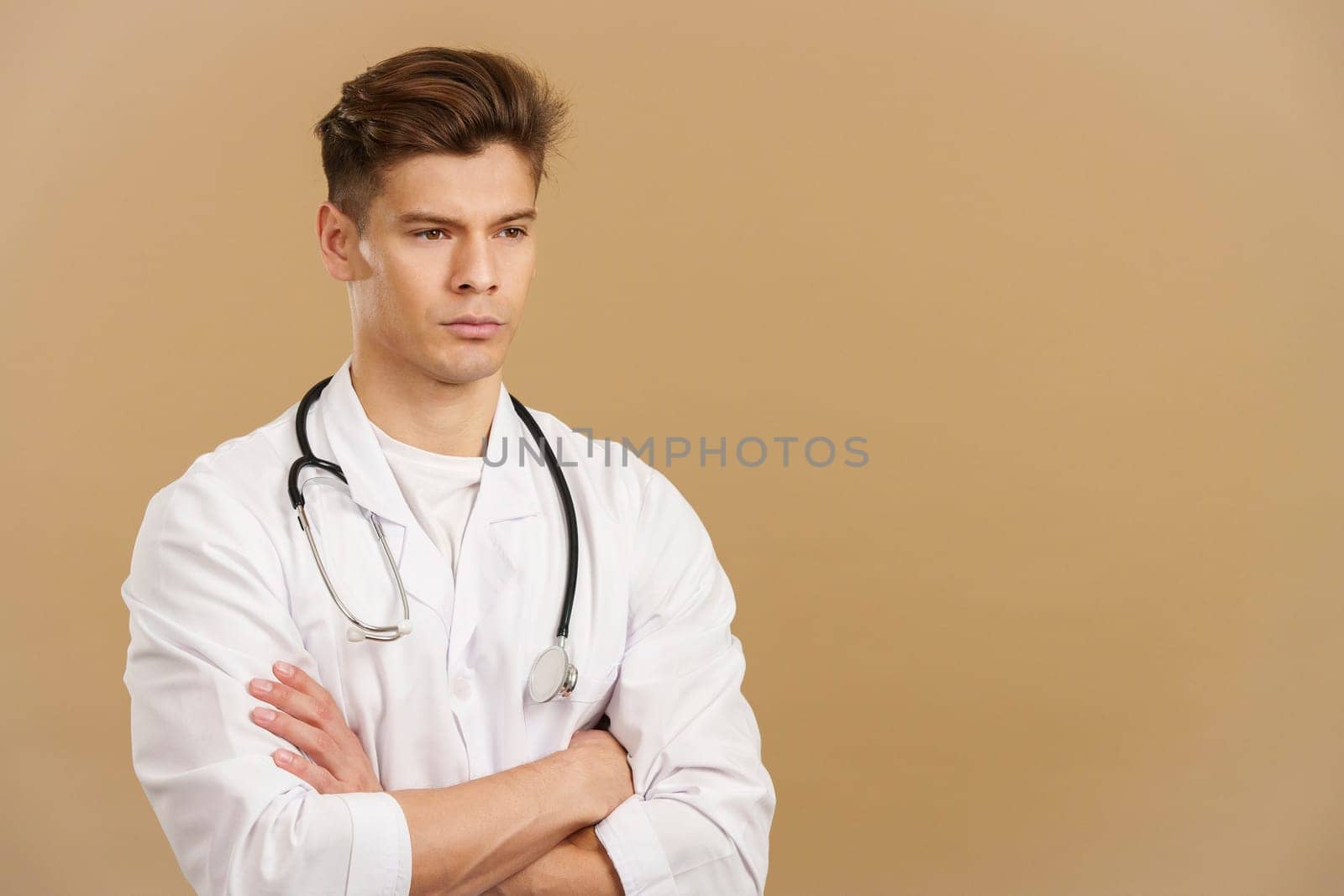 Serious doctor with arms crossed looking away in studio with brown background