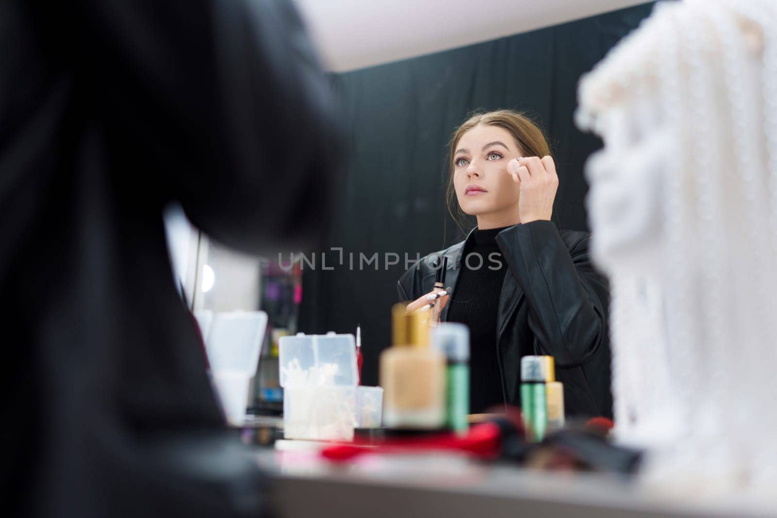 Low angle view photo of a caucasian beauty woman applying base make-up on her face backstage