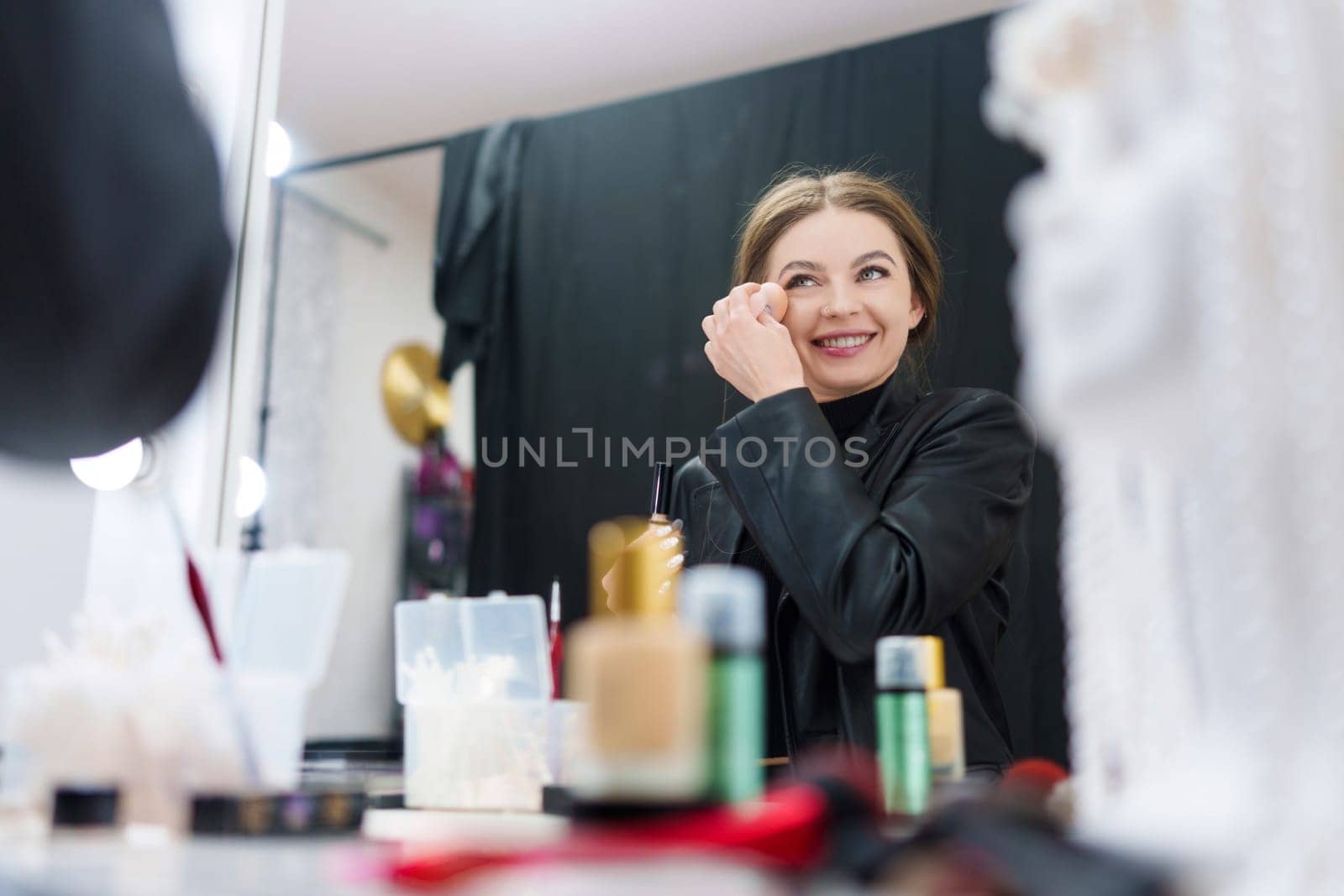 Reflection on the mirror of a woman applying powder while making up in a backstage