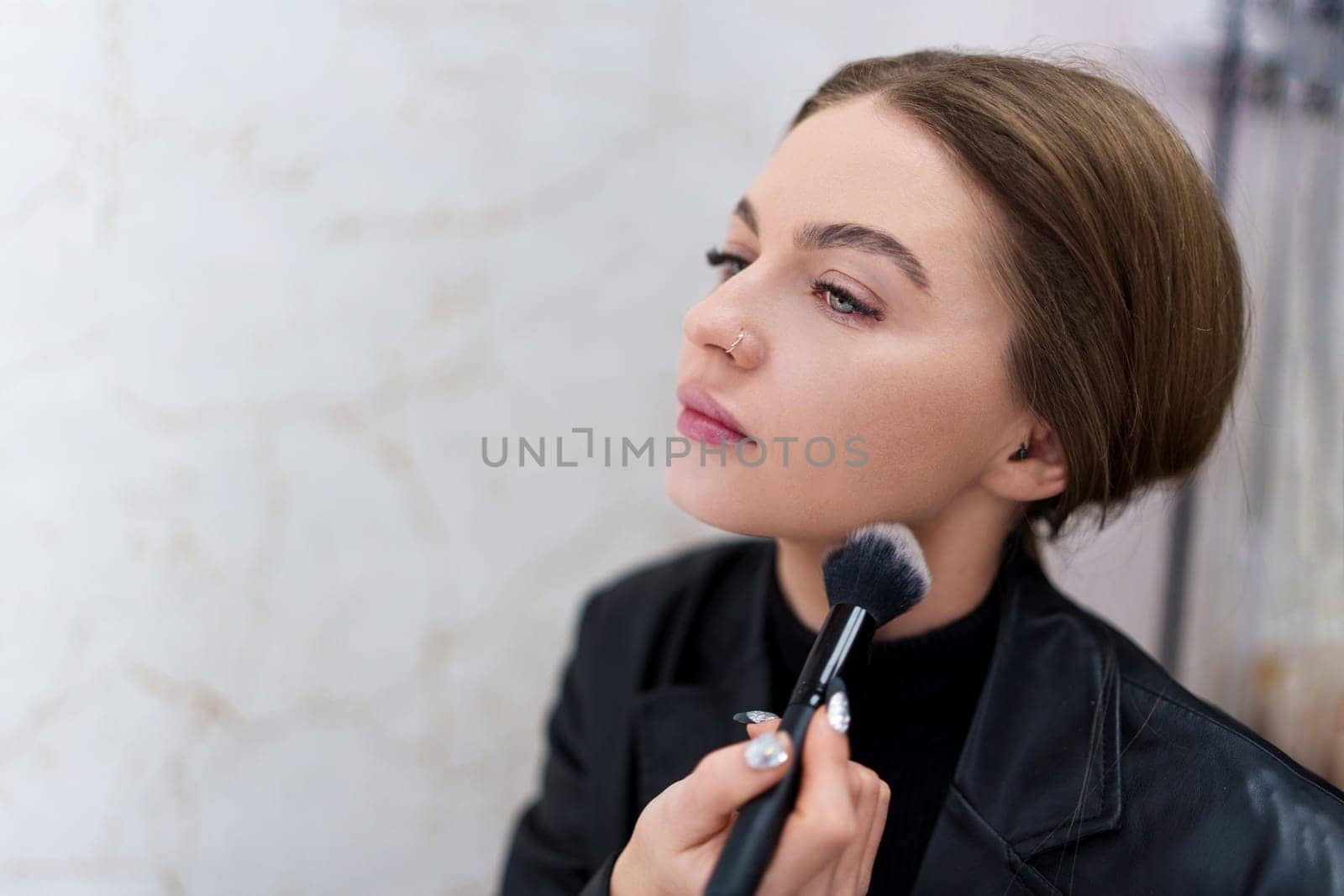 Close up portrait of a woman using a brush to make up in a backstage