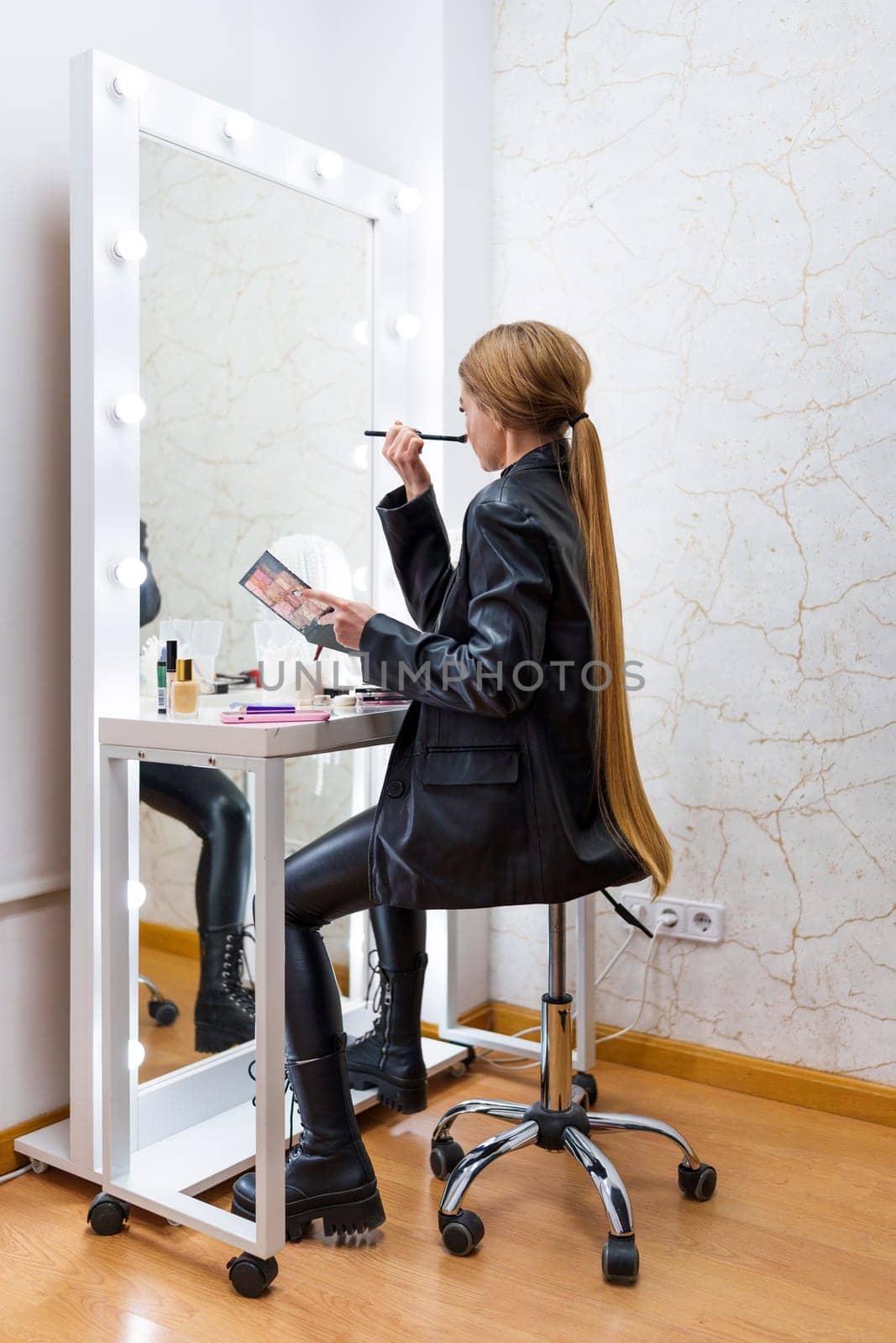 Vertical photo of the rear view of a woman using a brush to make up sitting on a backstage