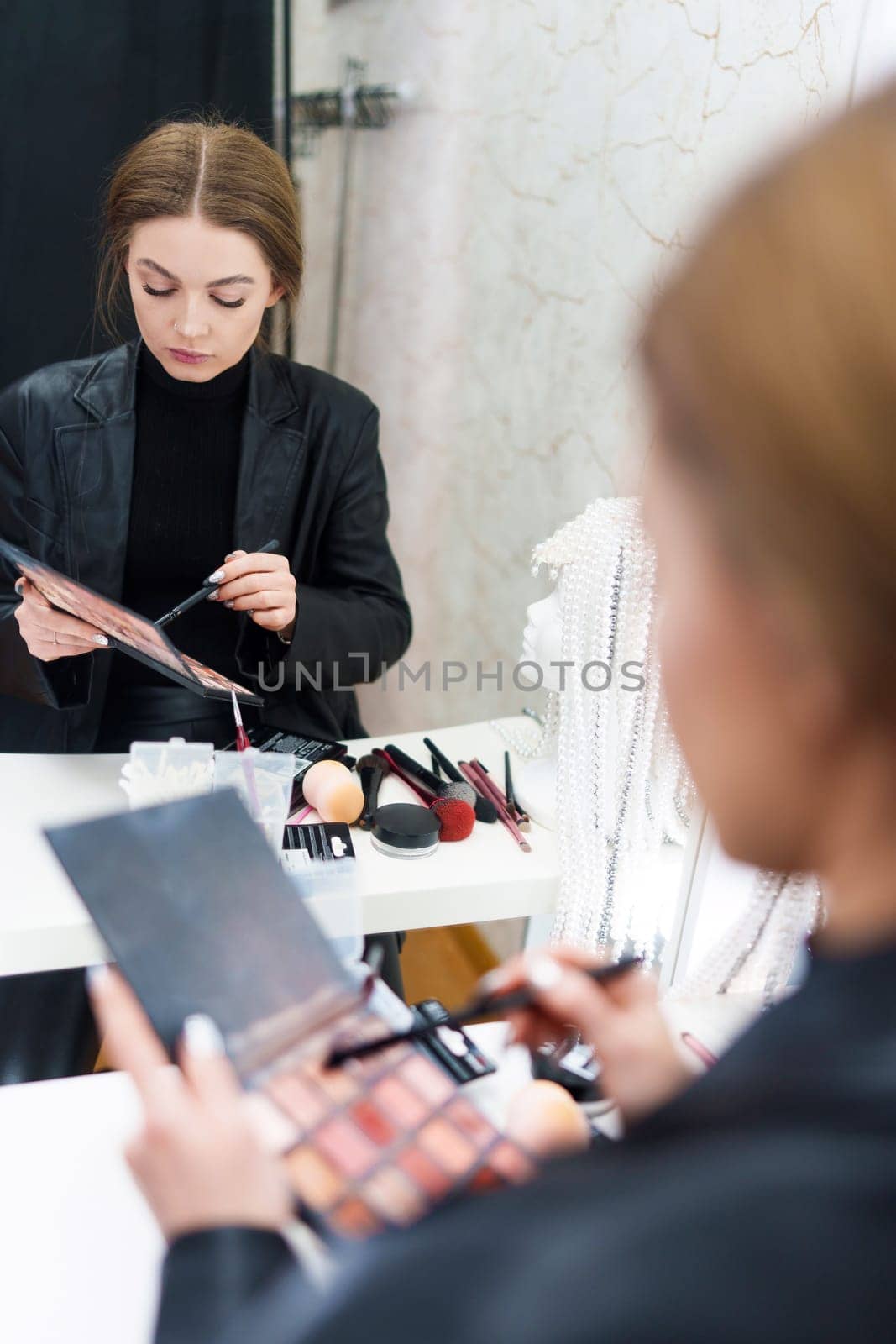 Vertical photo of the reflection on a mirror of a beauty woman making up in a backstage