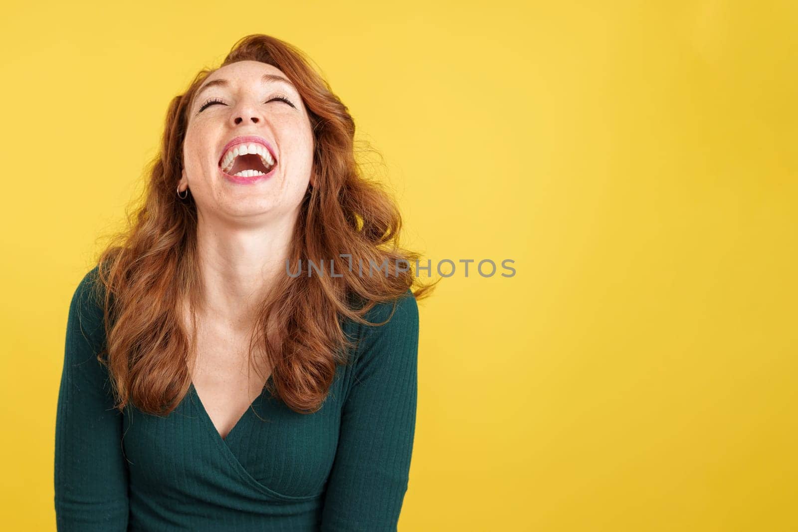 Happy redheaded woman laughing and looking up in studio with yellow background