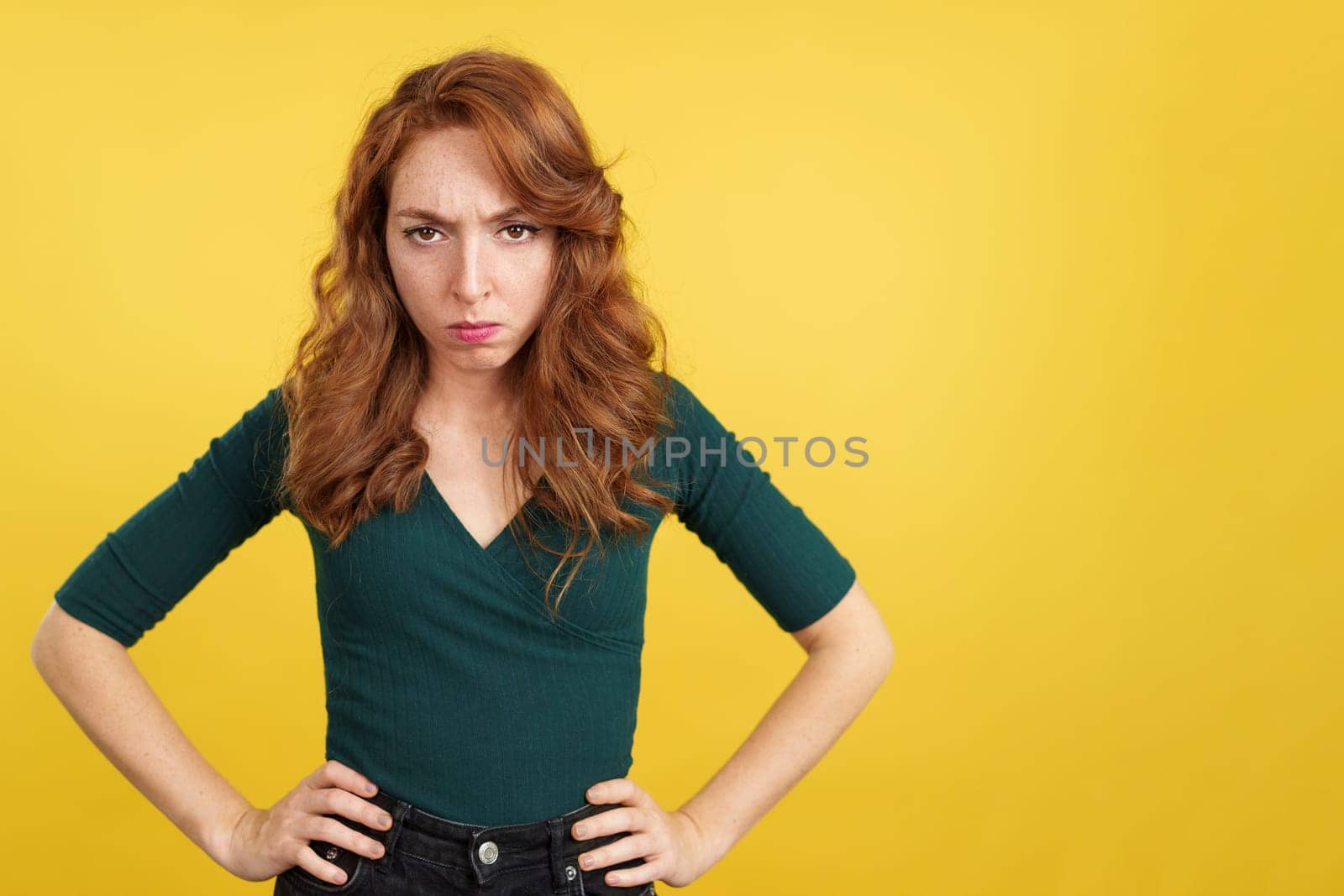 Redheaded woman looking at camera with an angry expression in studio with yellow background