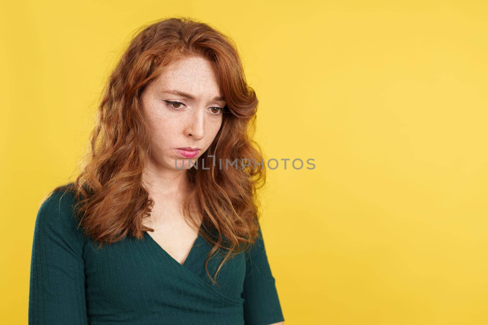 A depressed beauty redheaded woman looking down in studio with yellow background