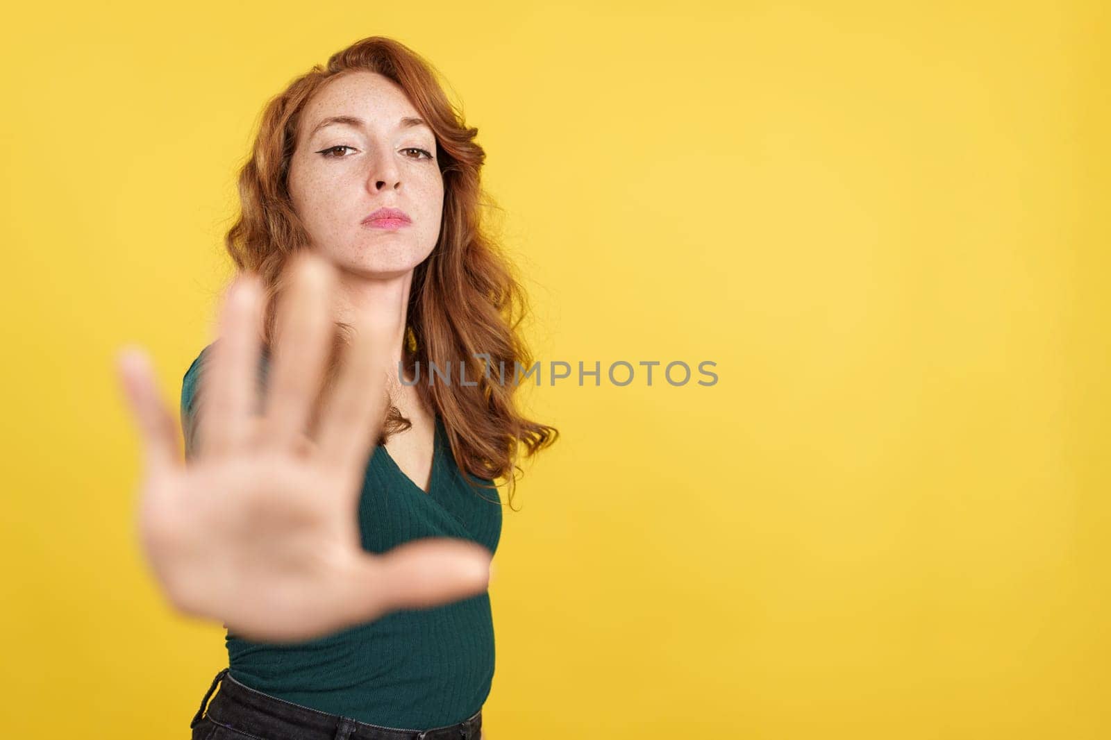 Redheaded woman gesturing prohibition with hand in studio with yellow background