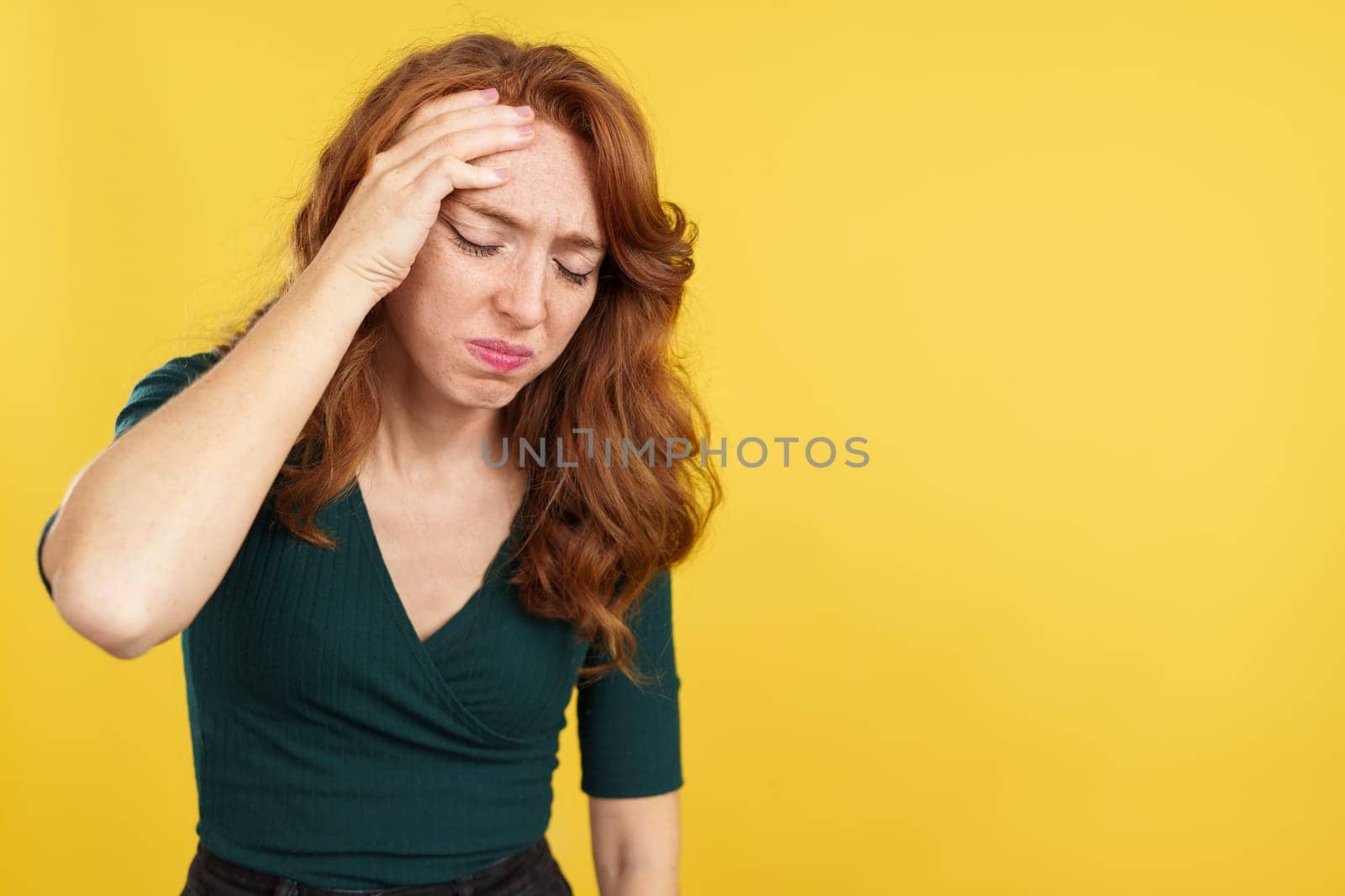 Beauty redheaded woman gesturing headache with the hand on head in studio with yellow background