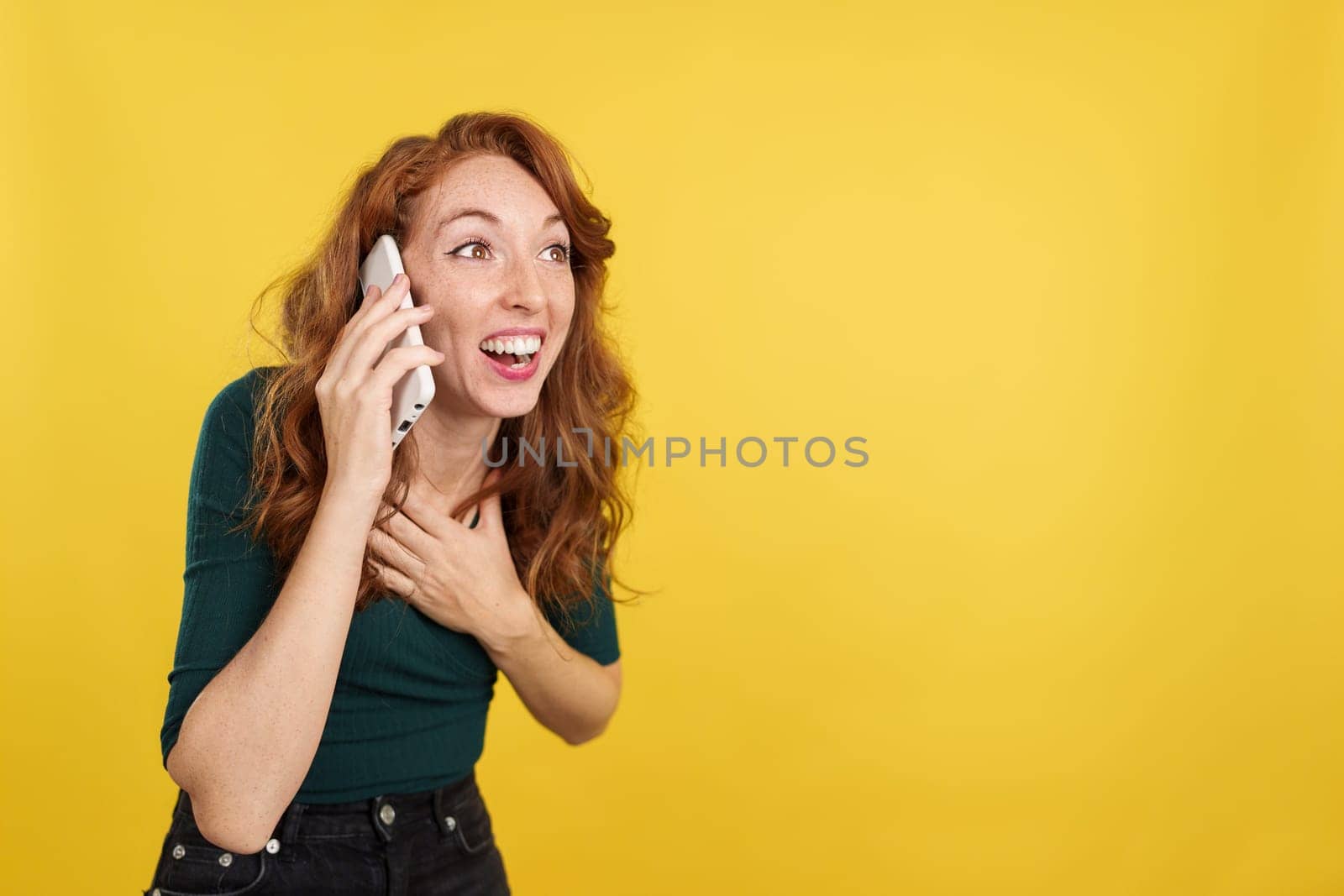 Redheaded woman receiving good news by mobile phone in studio with yellow background