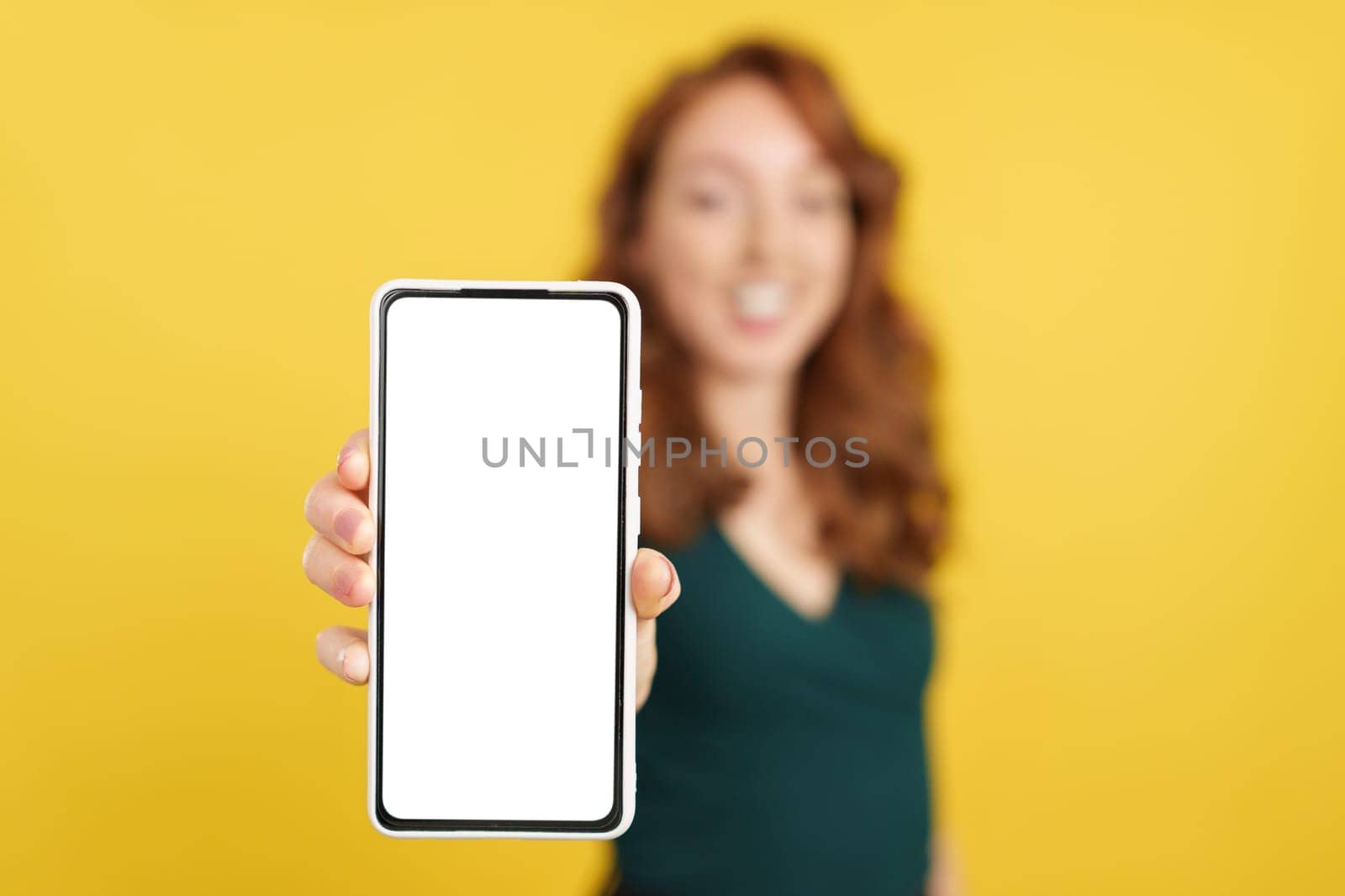 Blank screen of the mobile held by a redheaded woman in studio with yellow background