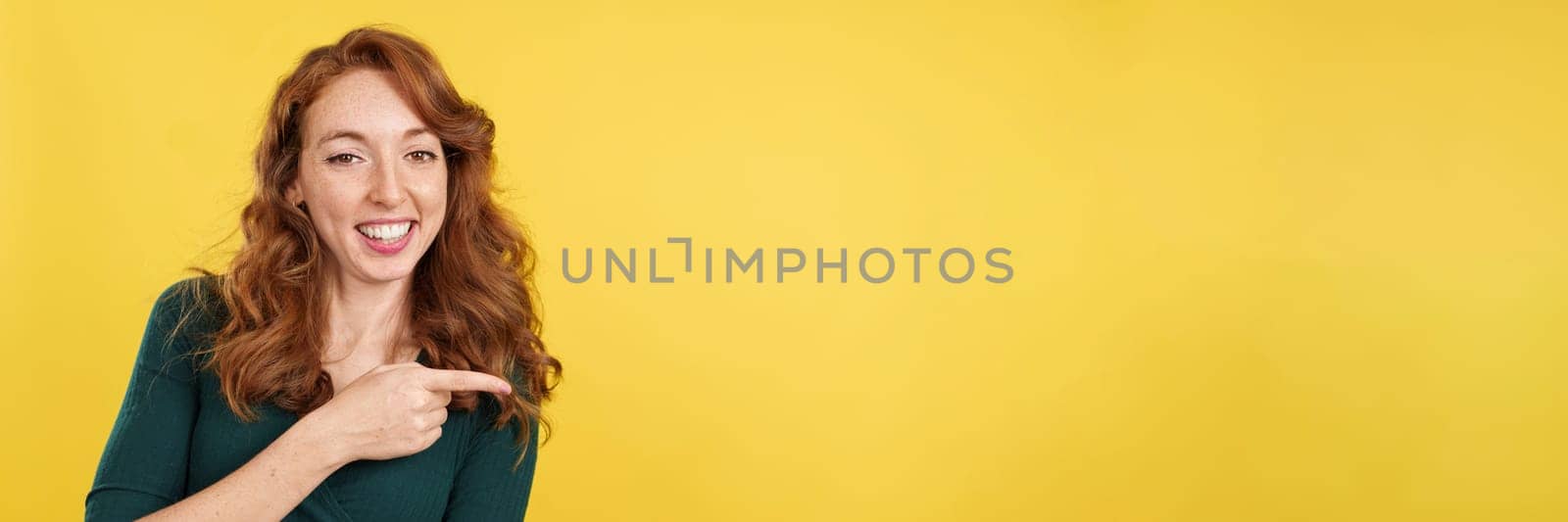Redheaded woman pointing a blank space and smiling by ivanmoreno