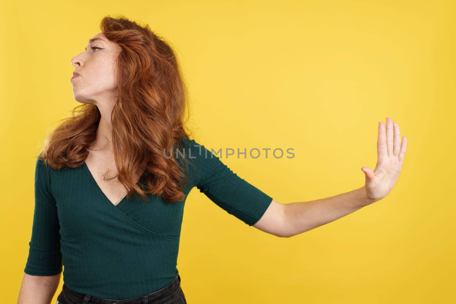 Angry redheaded woman reusing to talk gesturing with the hand in studio with yellow background