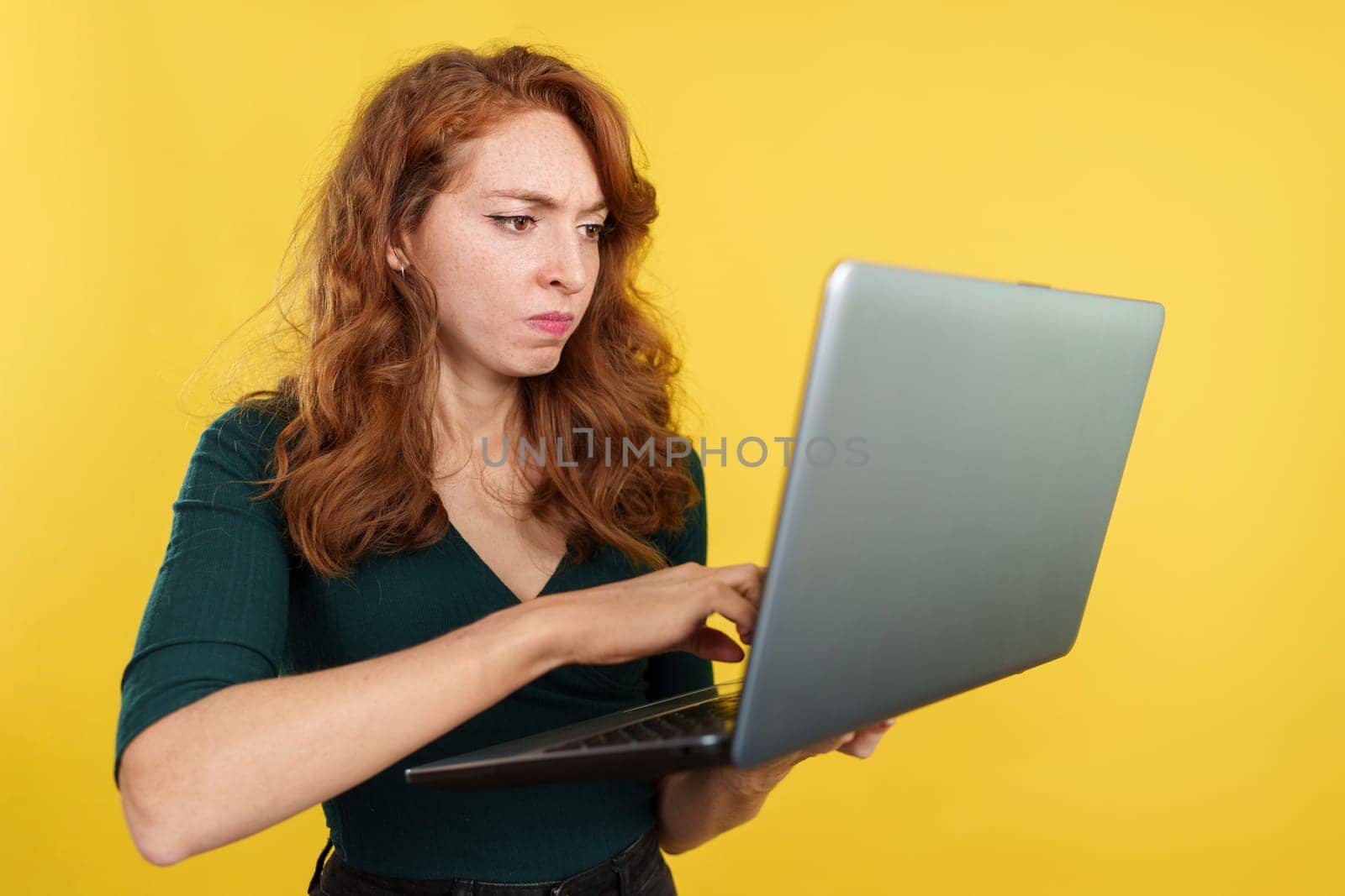 Redheaded woman having a problem with a laptop in studio with yellow background