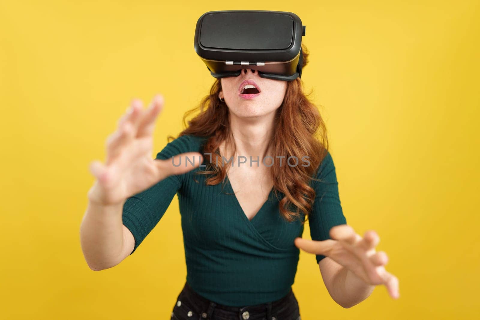 Amazed redheaded woman with Virtual Reality goggles in studio with yellow background