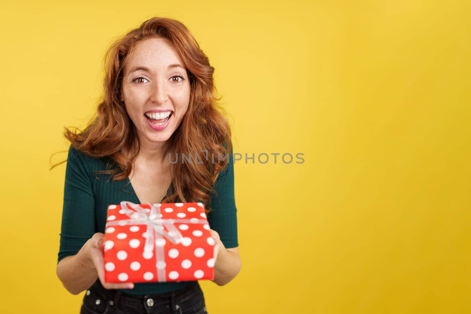 Redheaded woman smiling at camera with a gift in studio with yellow background