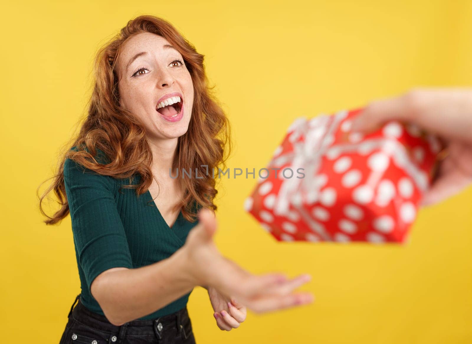 Cool redheaded woman smiling while receiving a gift in studio with yellow background