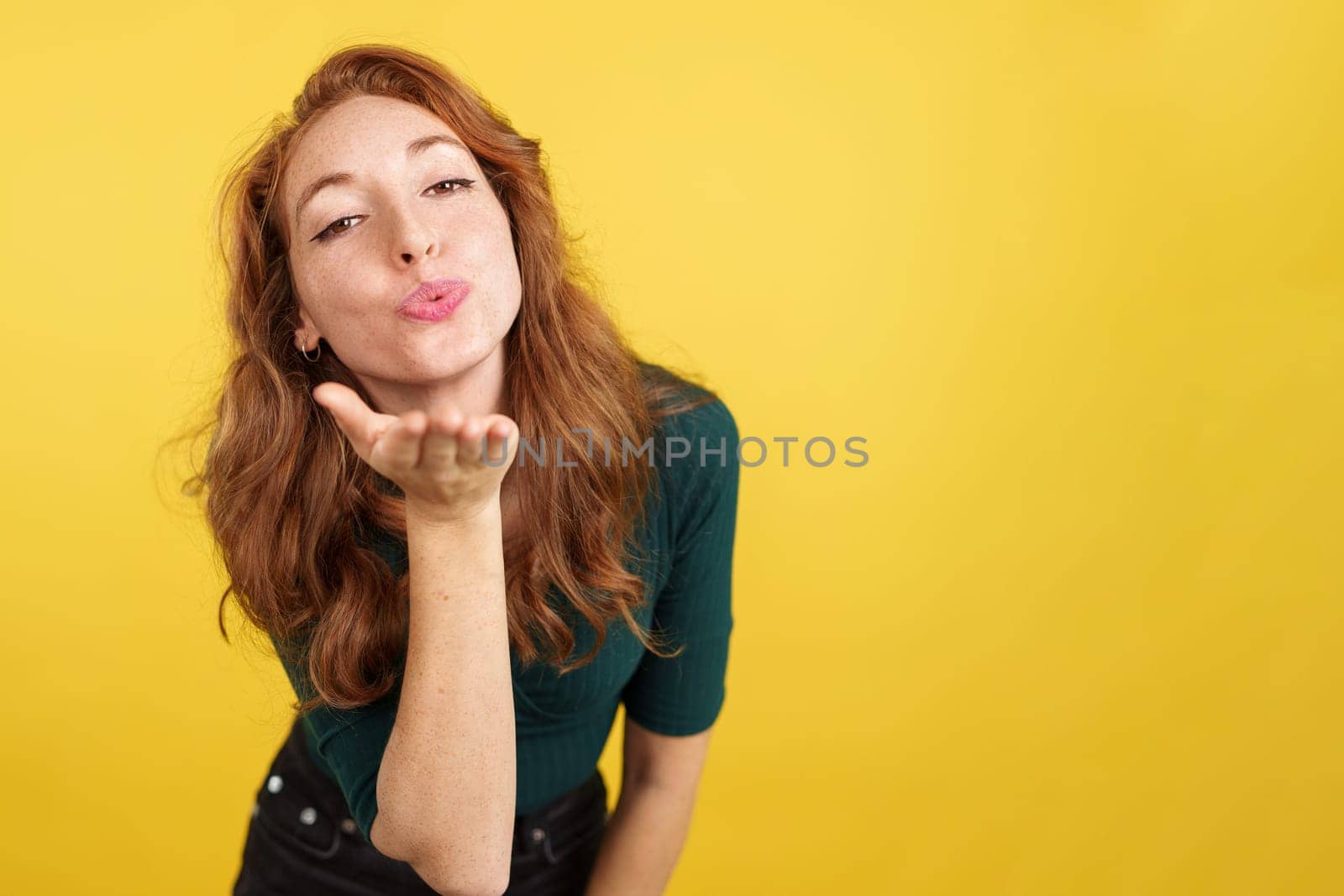 Redheaded woman blowing a kiss while looking at the camera in studio with yellow background