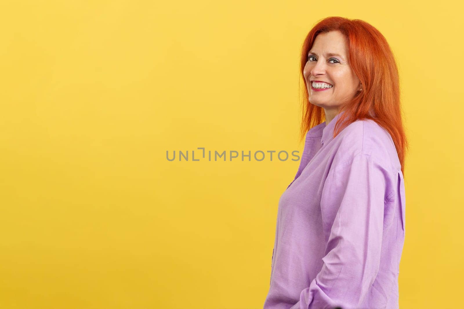 Happy redheaded mature woman smiling at the camera in studio with yellow background